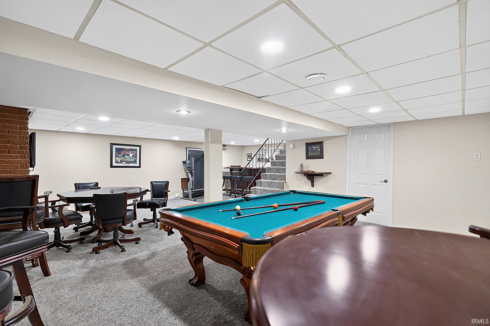 Finished lower level featuring a pool table, staircase with metal railing, recessed lighting, and light-colored carpeting