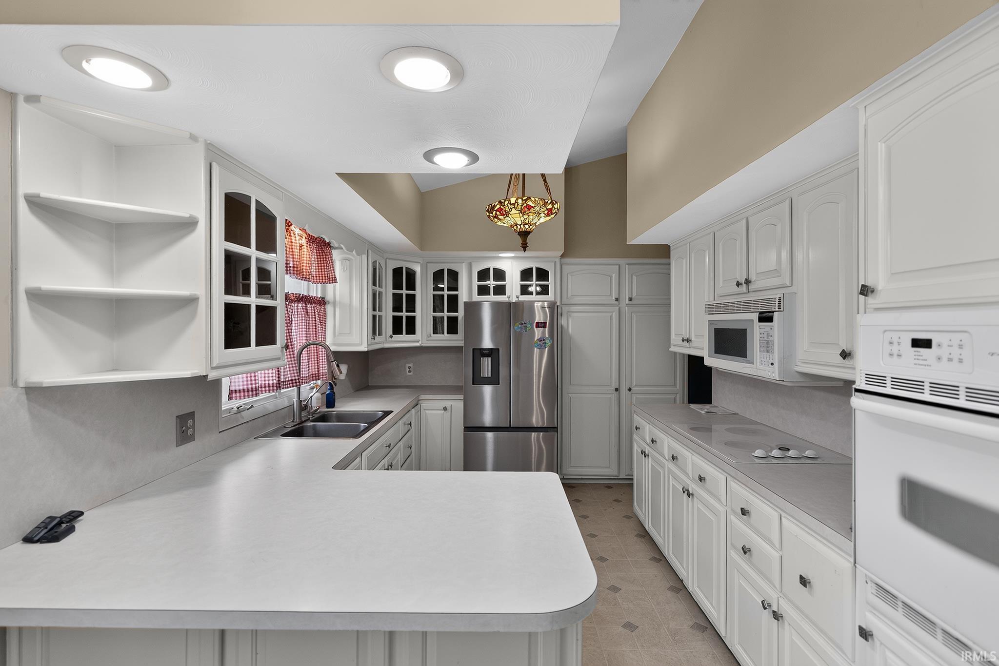 White cabinetry, white countertops, built-in appliances, stainless steel refrigerator, and recessed lighting