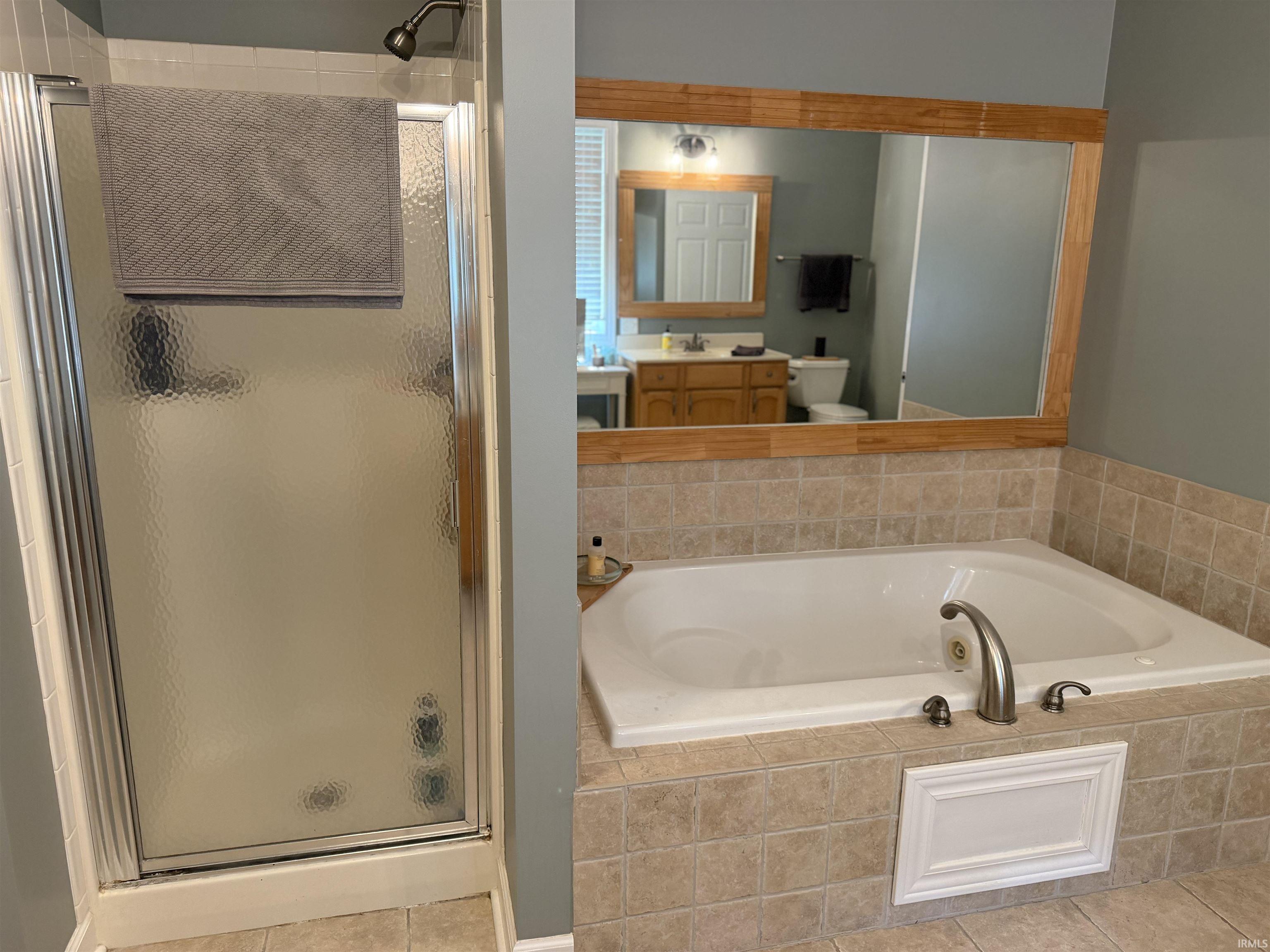 Bathroom featuring a tiled soaking tub with brushed nickel fixtures, a glass-enclosed shower, and a large mirror with a wood-finish frame
