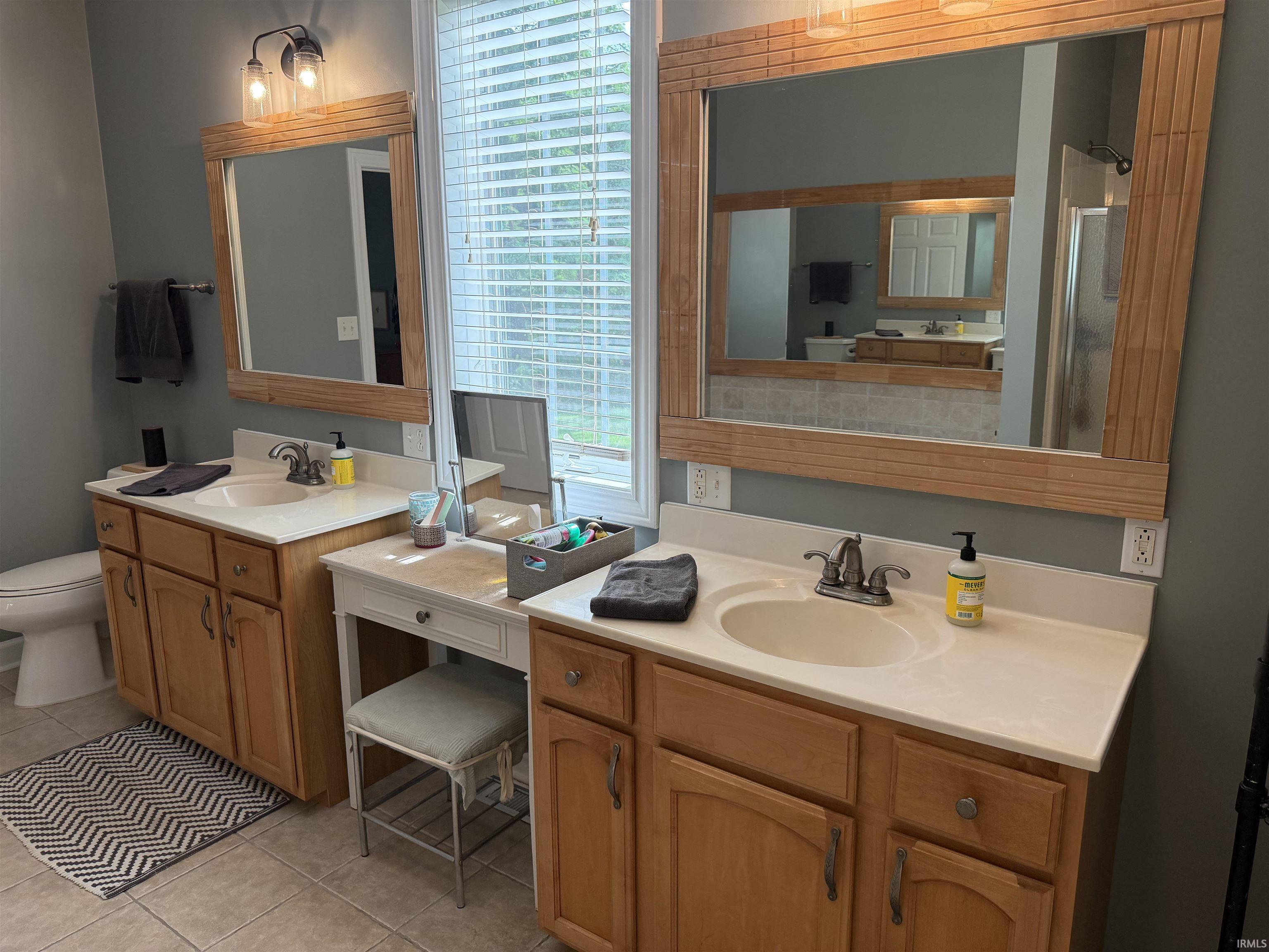 Bathroom featuring dual vanities with light wood cabinetry, integrated sinks, and neutral countertops