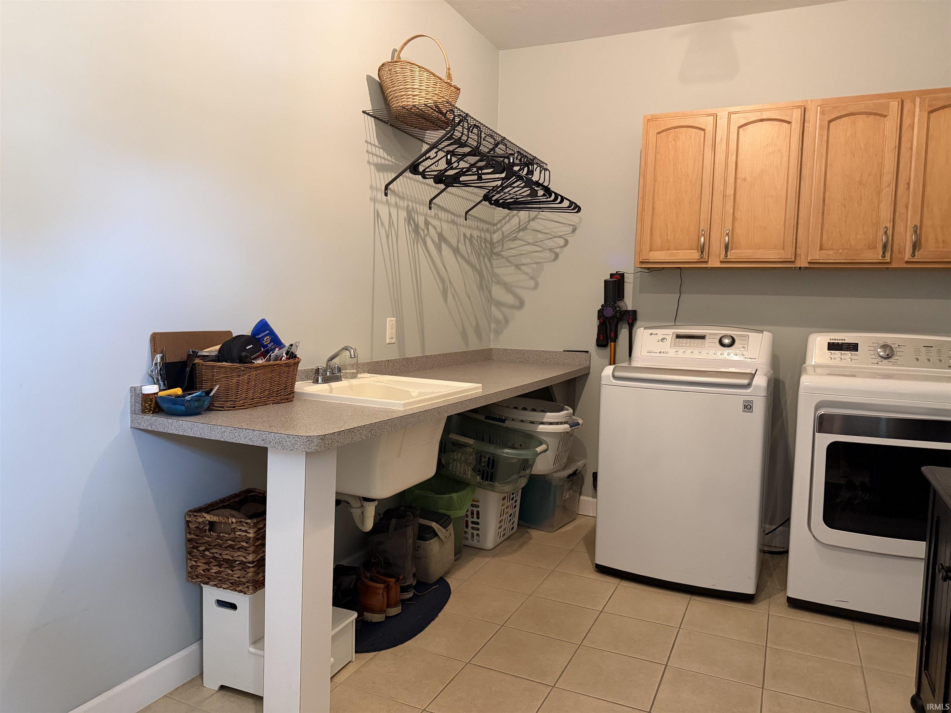 Laundry area featuring a utility sink, light-toned countertop, wood cabinetry, and neutral tile flooring