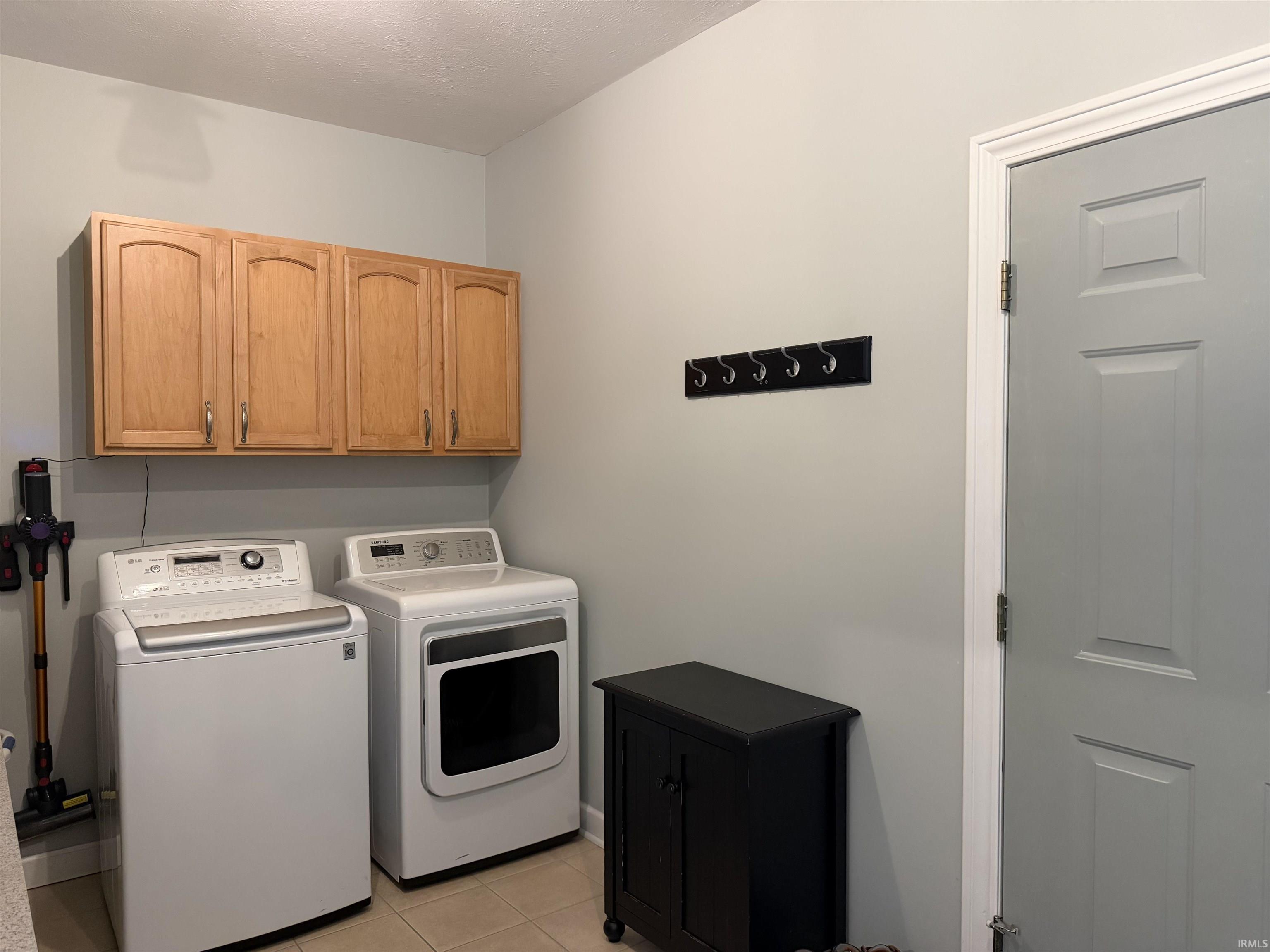 Laundry area featuring light wood-finish cabinetry, tile flooring, and a wall-mounted coat rack