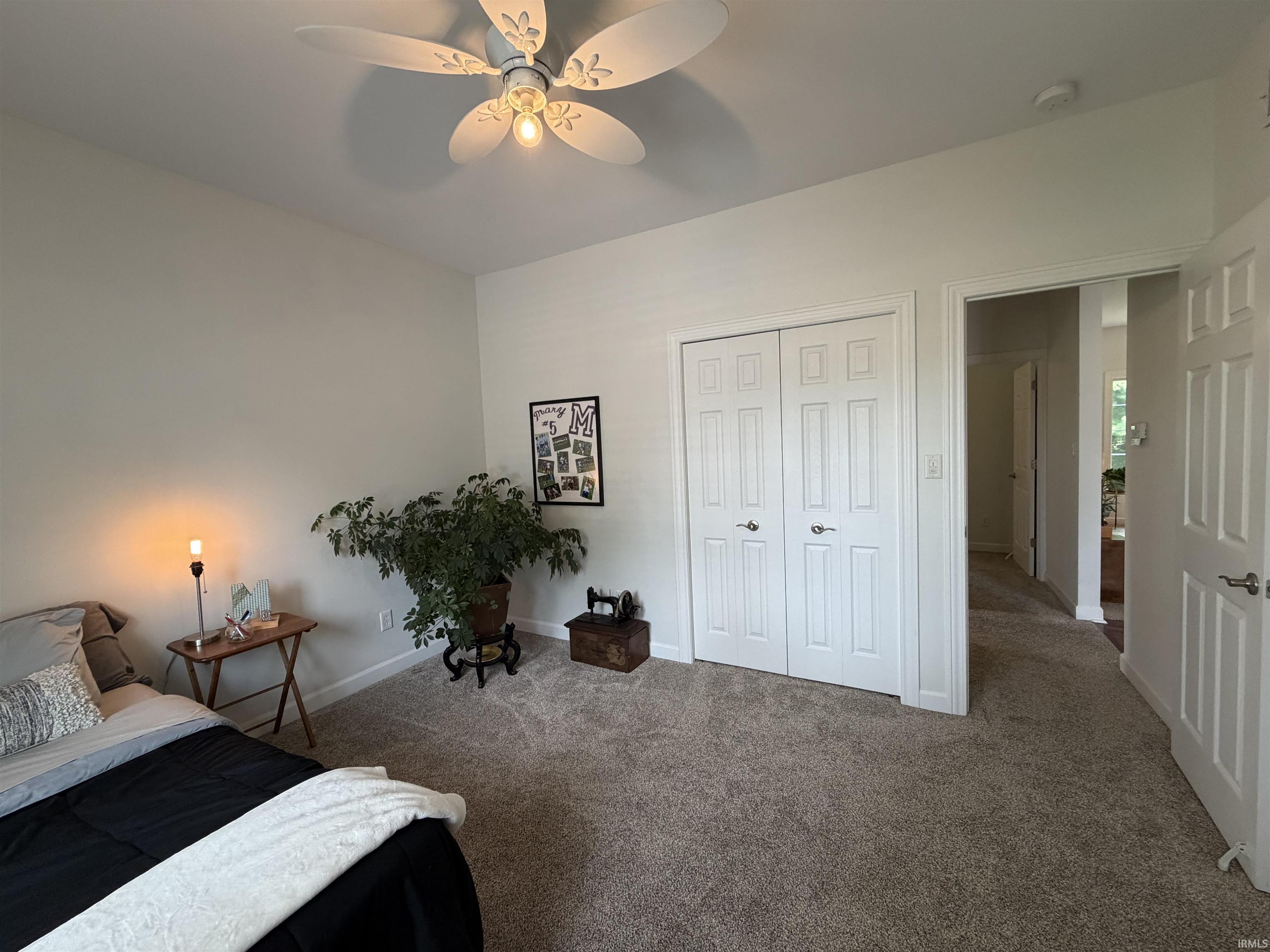 Carpeted room featuring a ceiling fan with integrated lighting, white baseboards, and a double-door closet with paneled doors and brushed nickel hardware