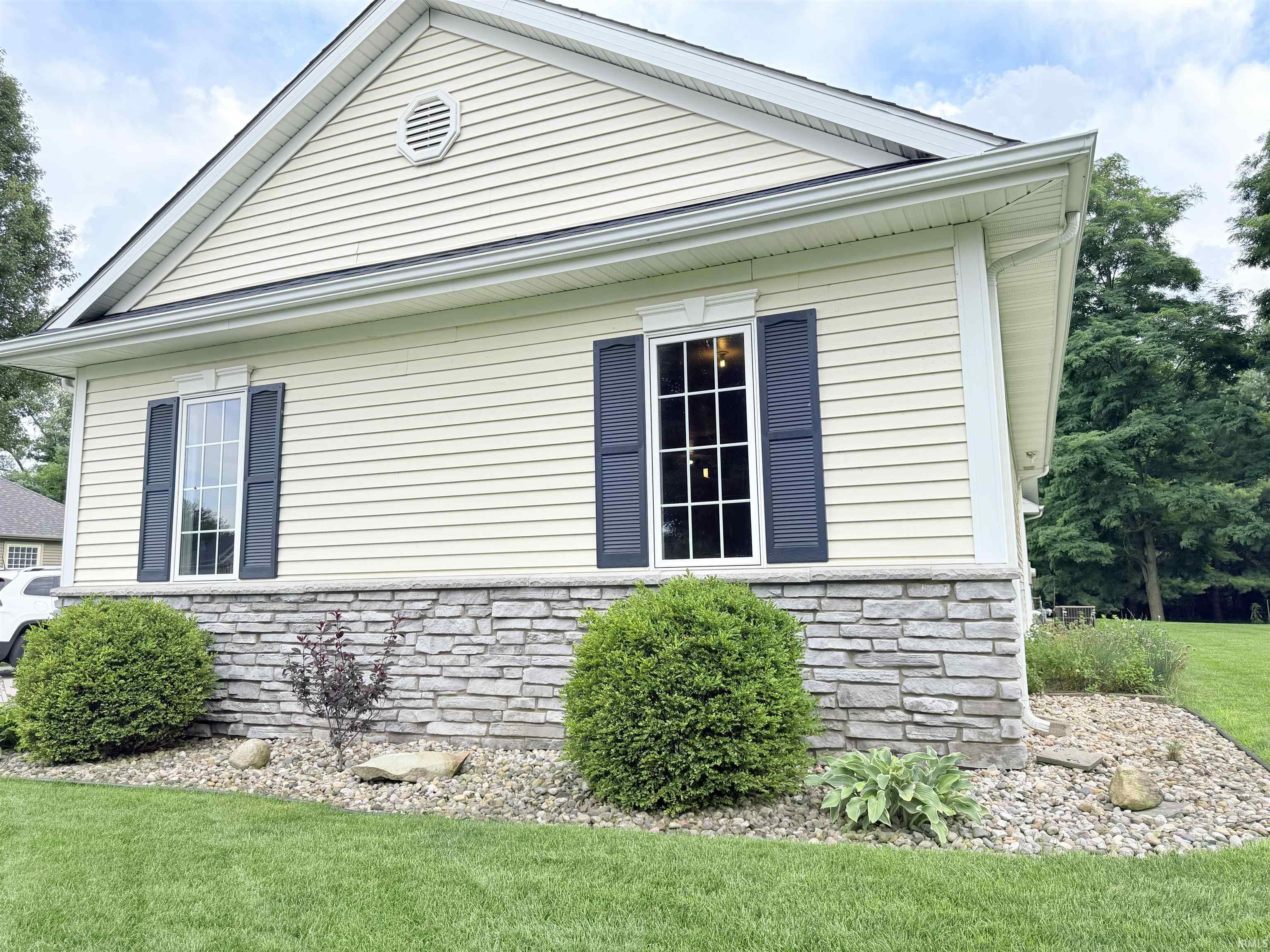 Exterior facade featuring light-colored siding, a stone veneer foundation, and dark louvered shutters