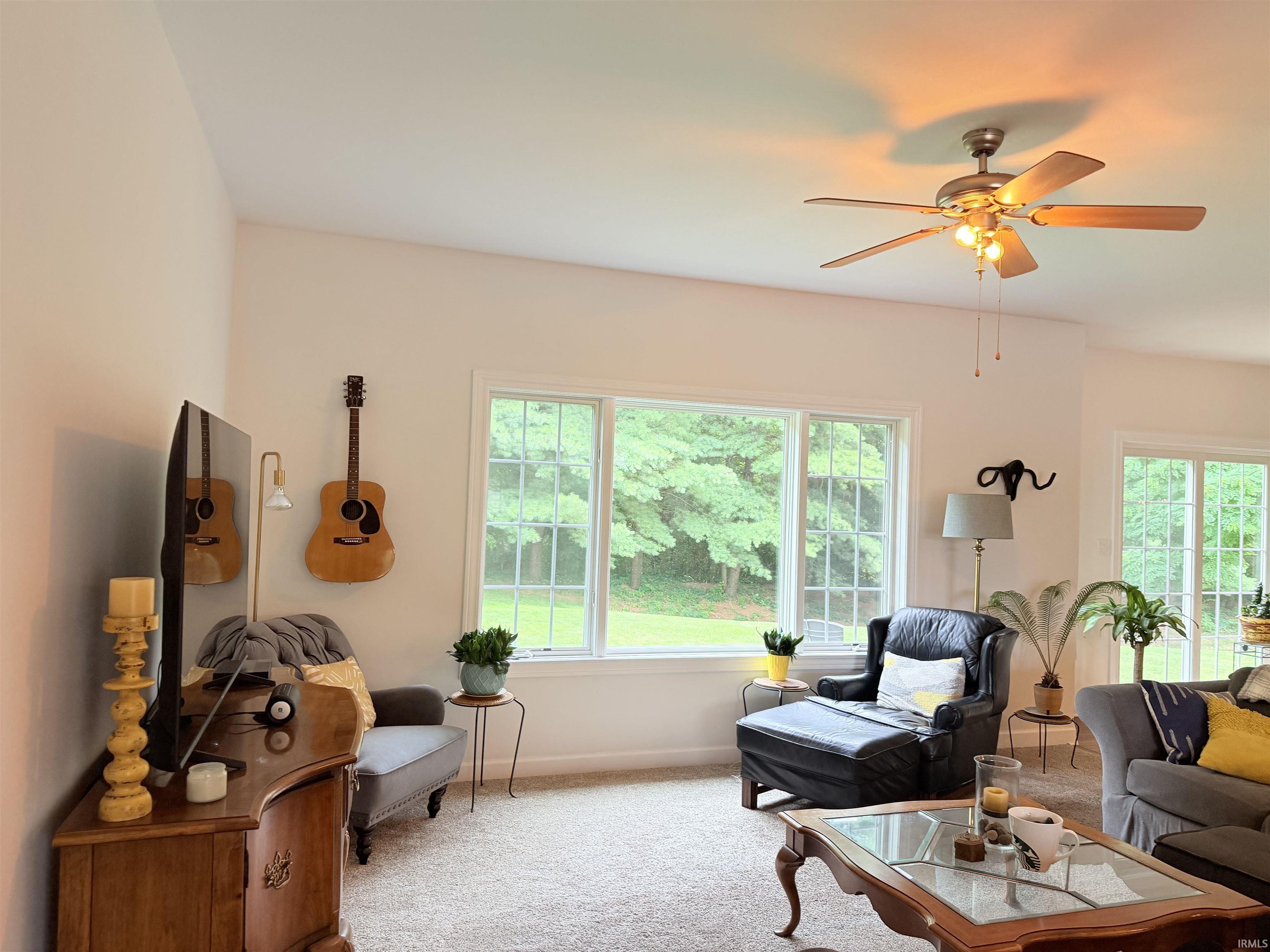 Spacious living area featuring large windows, a sliding glass door, a ceiling fan with integrated lighting, and neutral carpeting