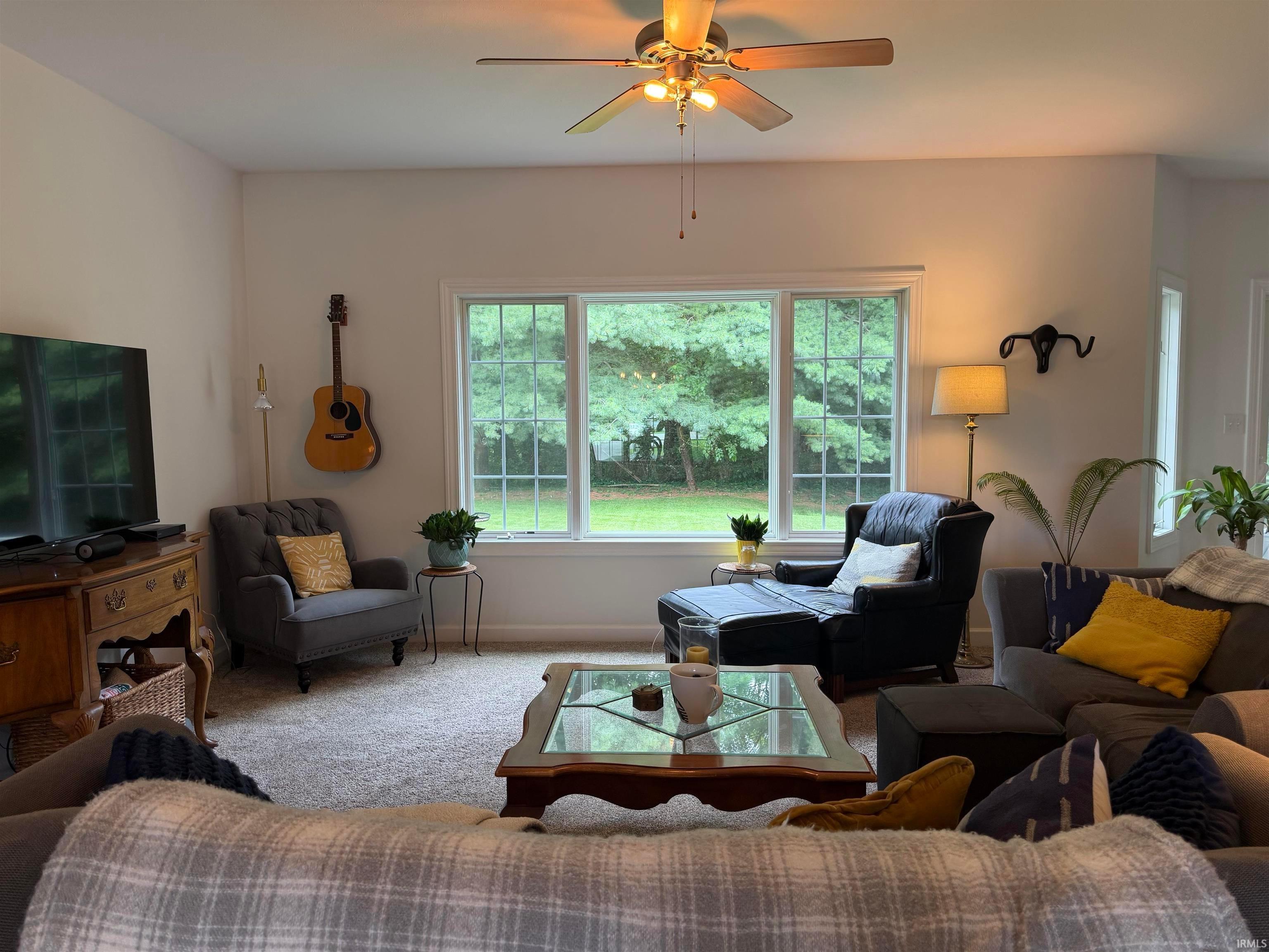 Bright living area featuring a large window overlooking lush greenery, a ceiling fan with integrated lighting, and neutral wall tones