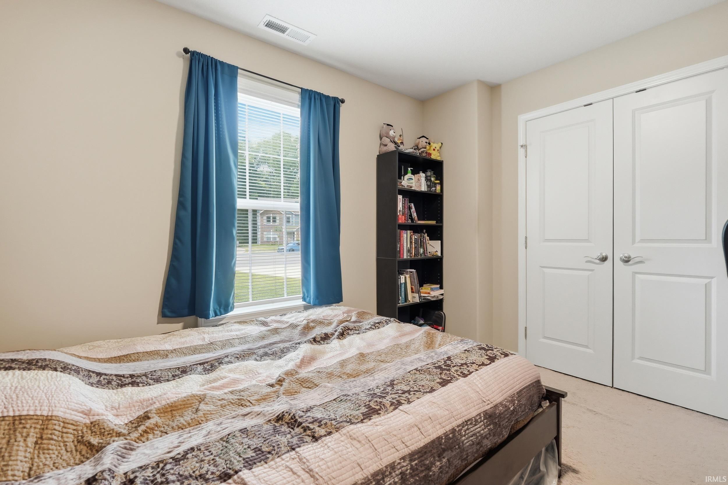 Bright bedroom featuring a window with blinds, neutral wall paint, and light-colored carpet flooring