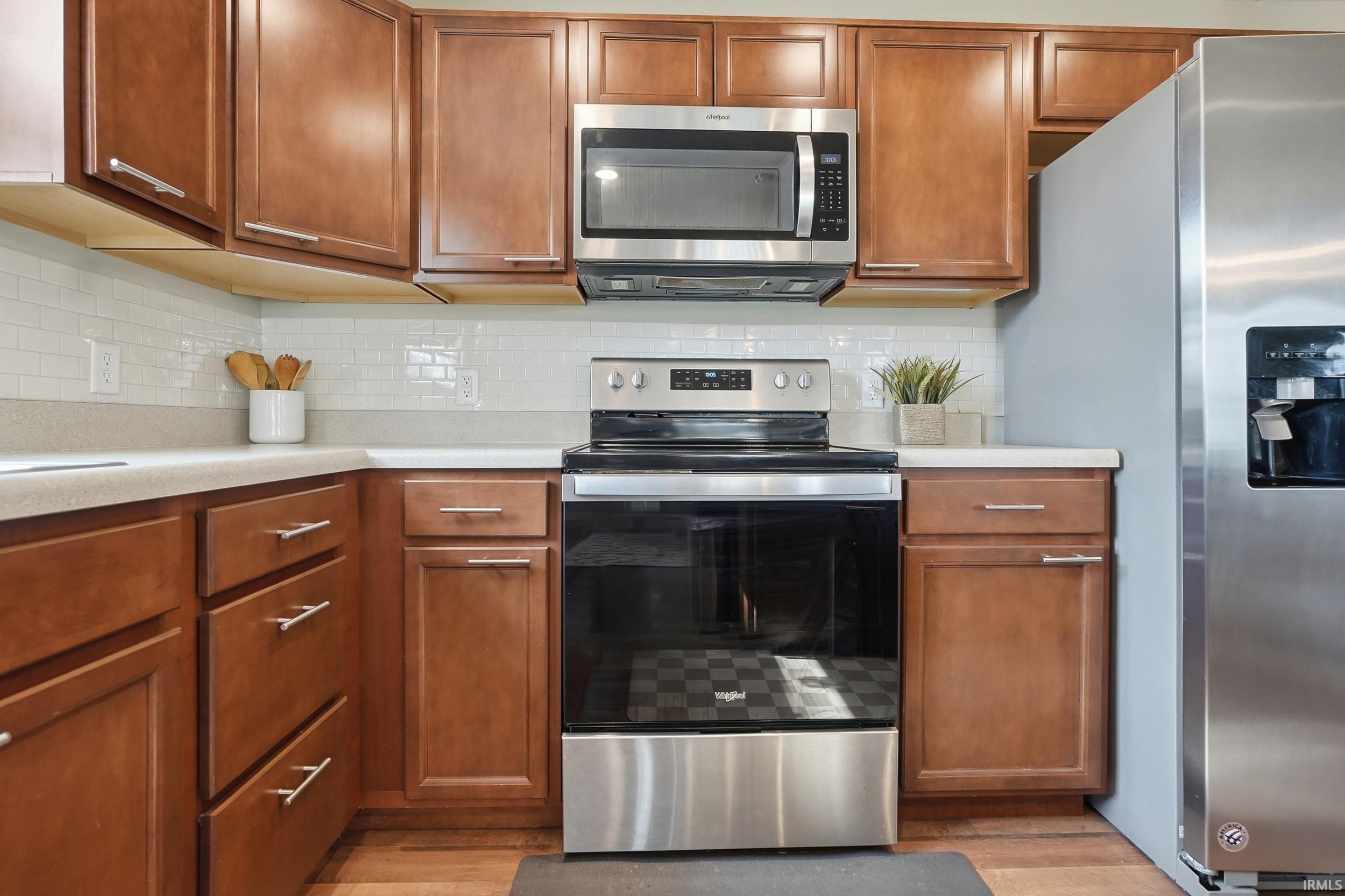 Kitchen featuring stainless steel appliances, wood-finish cabinetry, light-toned countertops, and a white subway tile backsplash