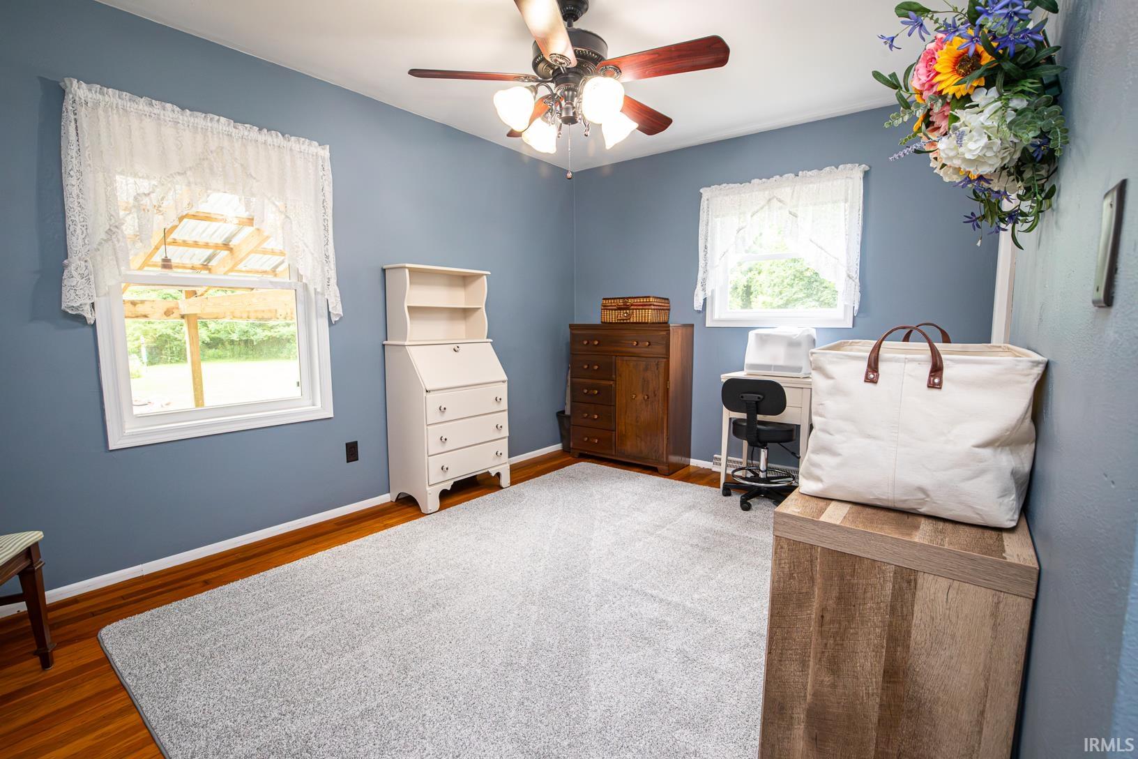 Room featuring two windows with white trim, wood-finish flooring, and a ceiling fan with integrated lighting