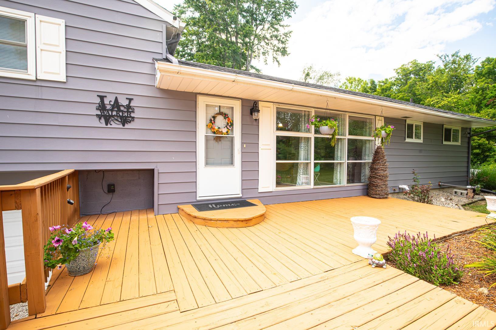 Expansive outdoor deck featuring wood-finish flooring, a white entry door, and large picture windows