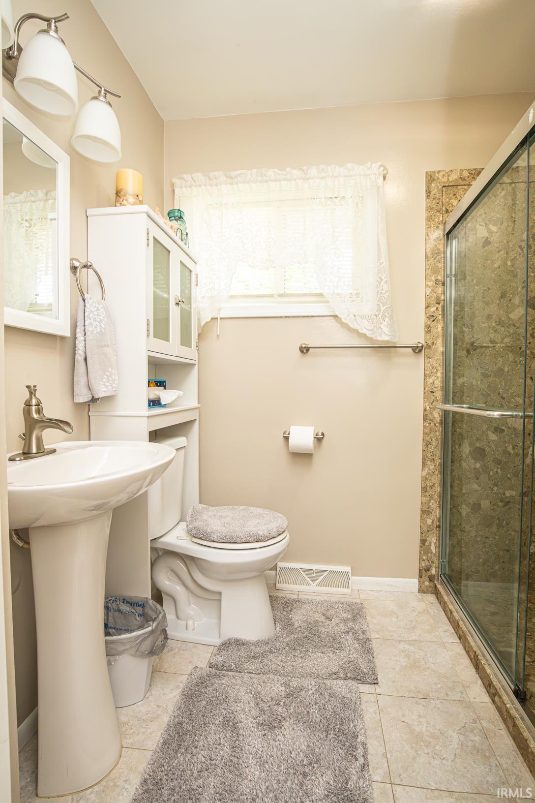 Bathroom featuring a pedestal sink, a glass-enclosed shower with tiled surround, and a window with natural light