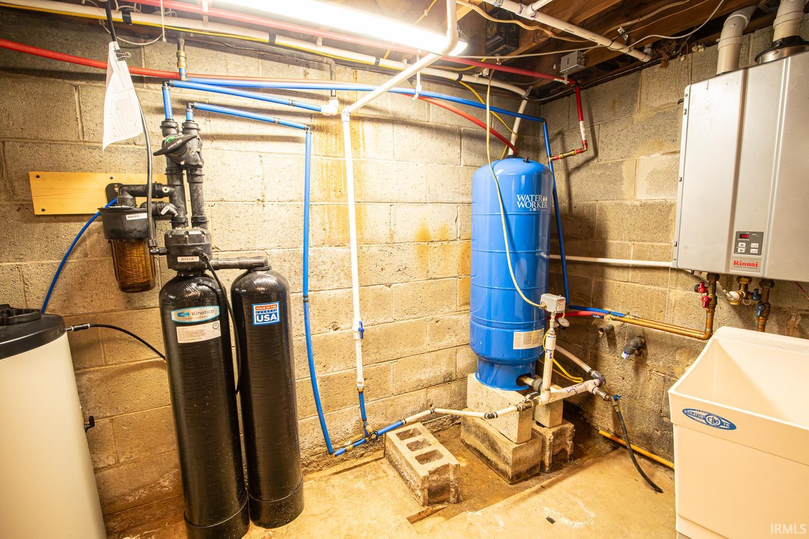 Utility area featuring a tankless water heater, water treatment system, pressure tank, and a utility sink