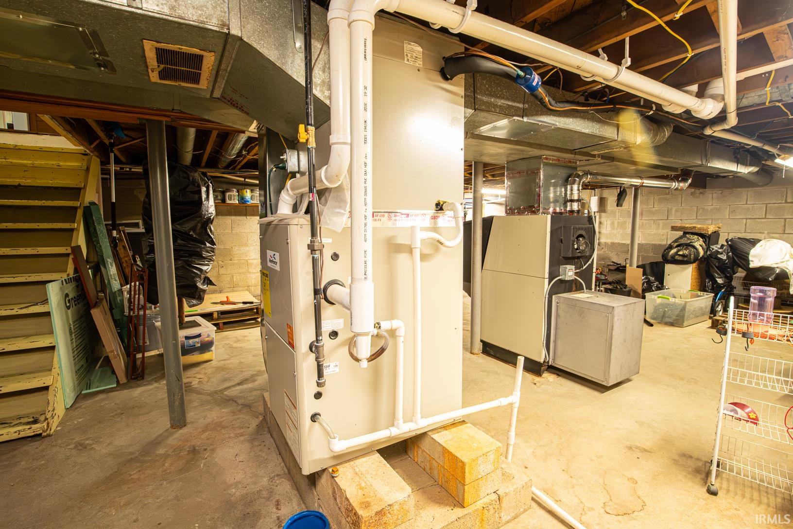 Concrete basement flooring with exposed ceiling joists and ductwork, featuring a central HVAC system and utility water heater