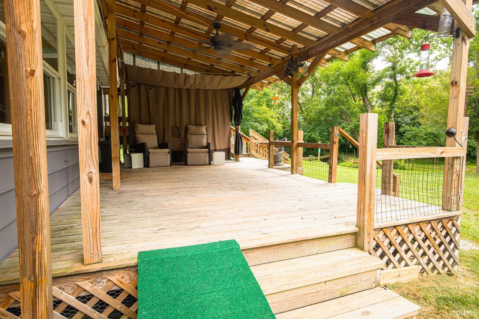 Expansive covered wood deck featuring a clear panel roof, ceiling fan, and privacy curtains