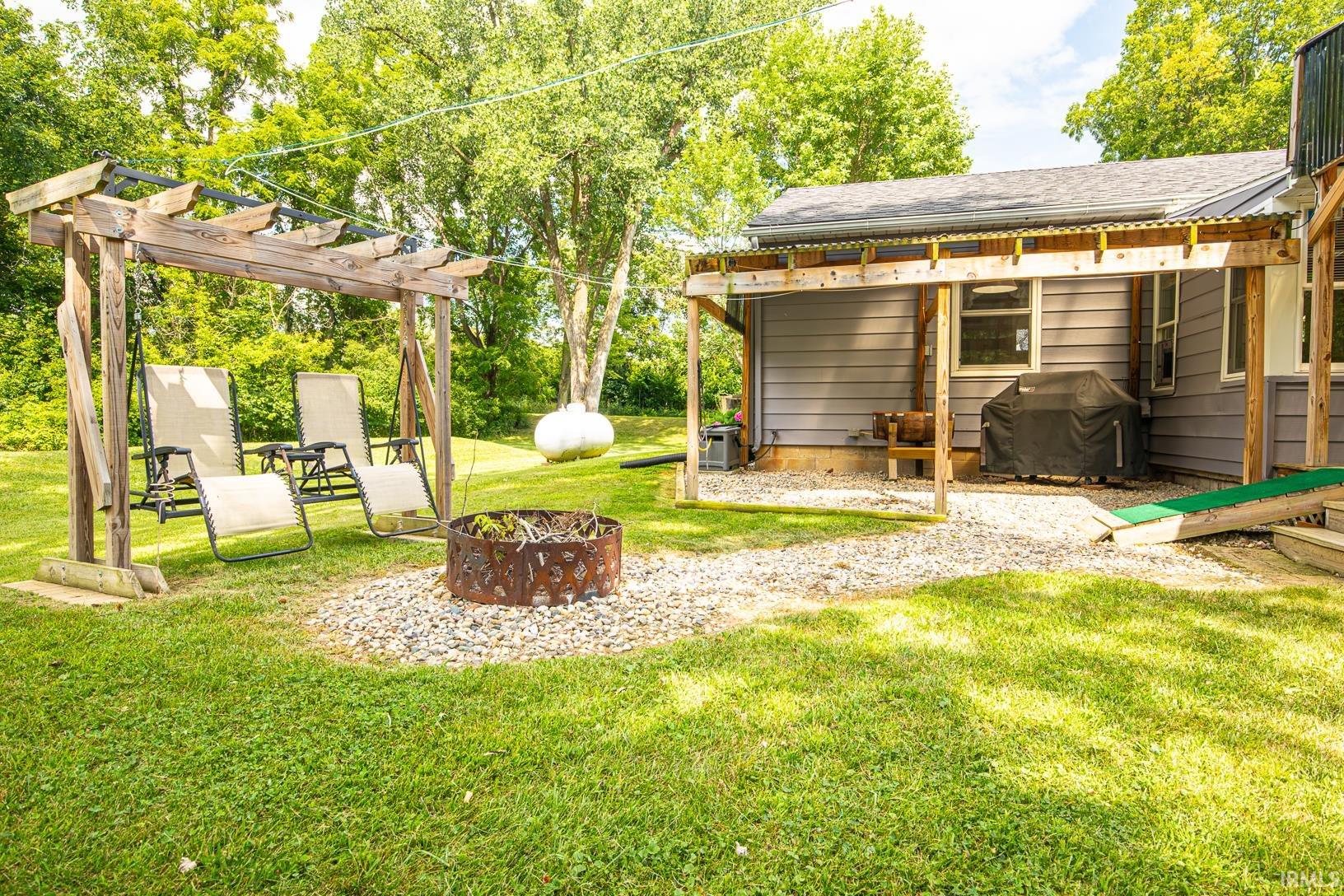 Expansive backyard featuring a pergola, gravel patio, wood-sided residence, and mature trees