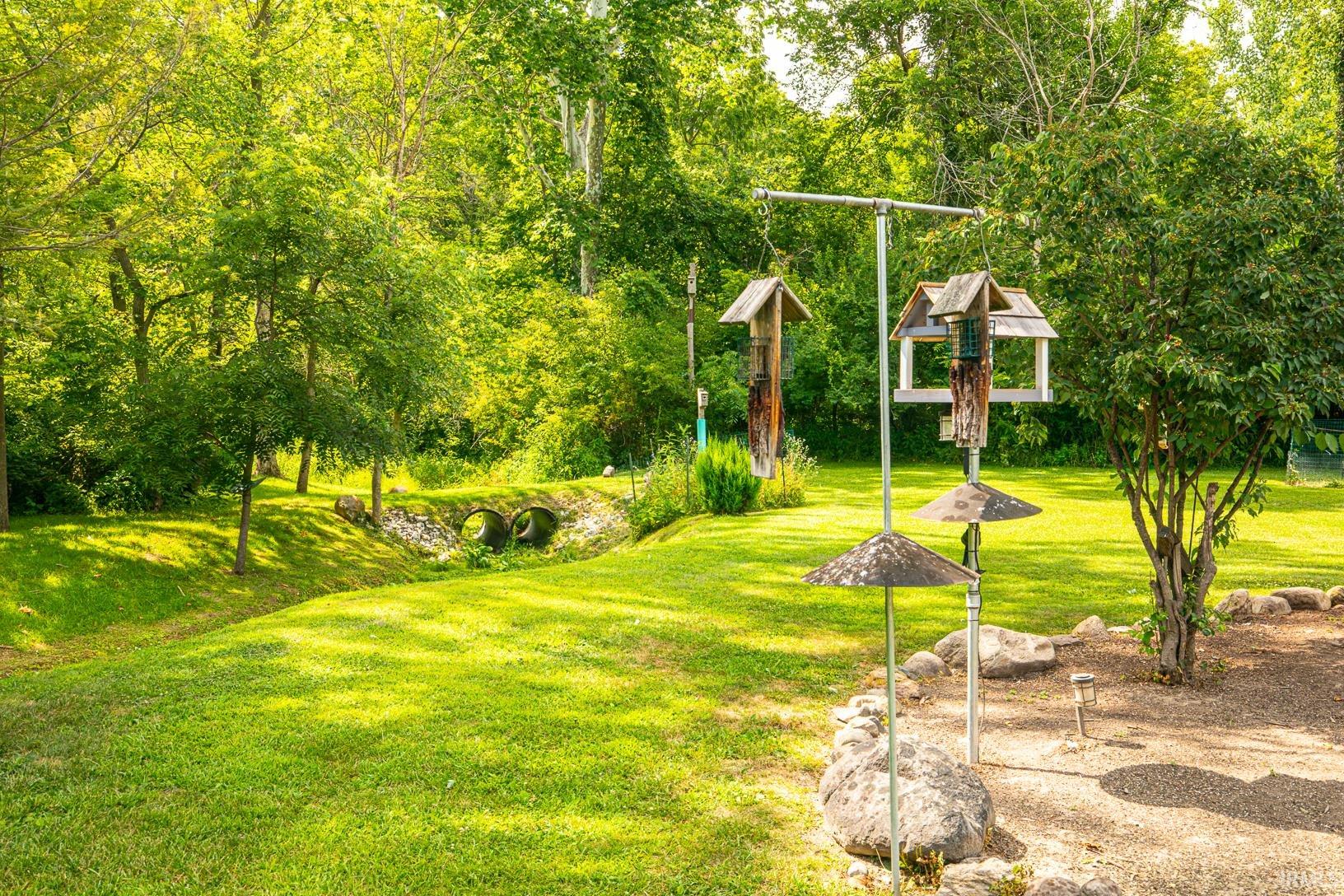 Expansive green lawn surrounded by mature trees, featuring a stone bridge over a natural stream