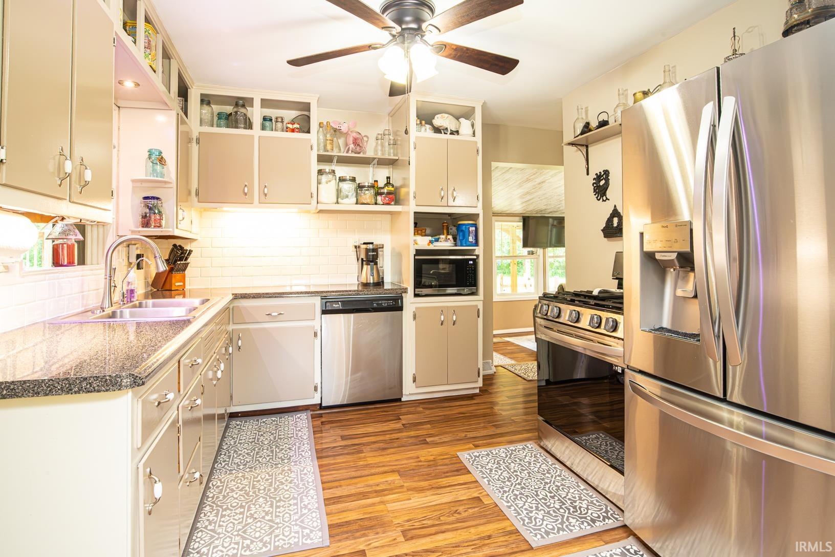 Kitchen featuring wood-finish flooring, stainless steel appliances, light-toned cabinetry, a subway tile backsplash, and a ceiling fan