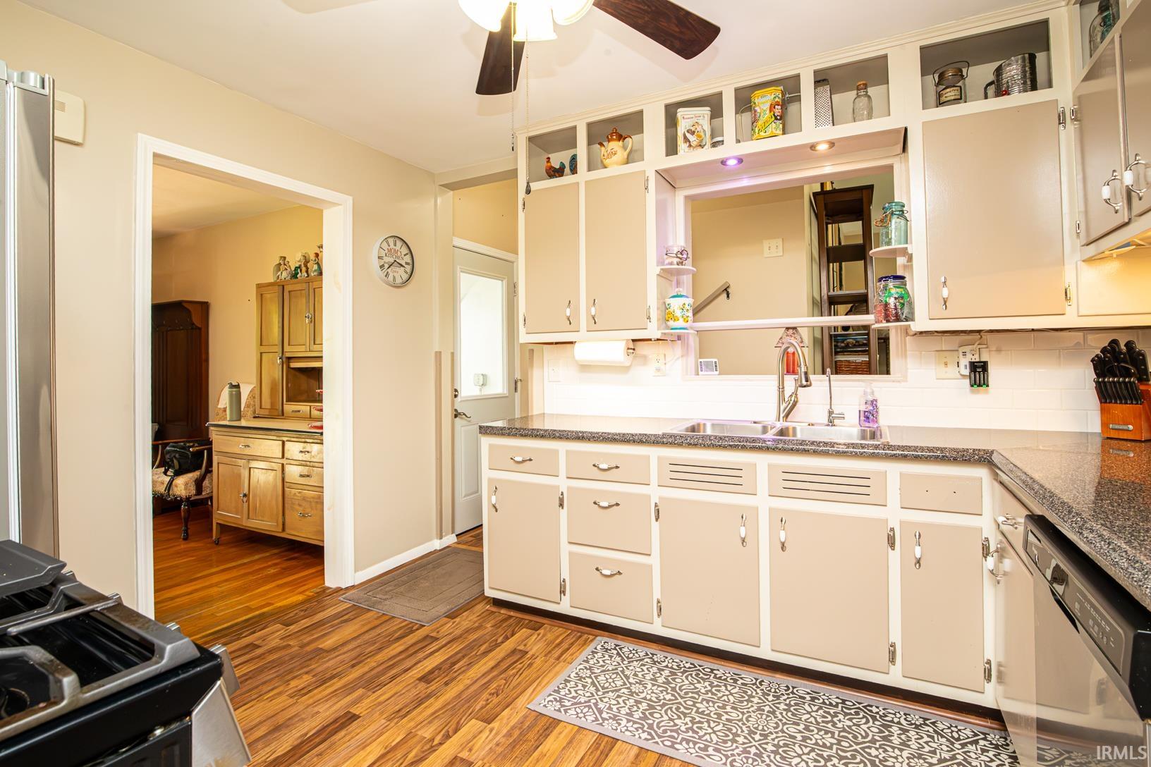 Kitchen featuring wood-finish flooring, light-toned cabinetry, a stainless steel sink with a gooseneck faucet, and a pass-through window with display shelving