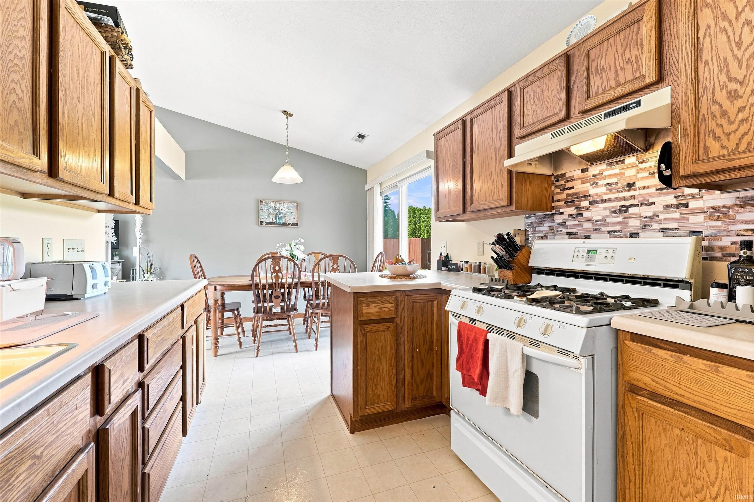 Kitchen featuring wood-finish cabinetry, a gas range with an overhead microwave/vent, and a patterned tile backsplash