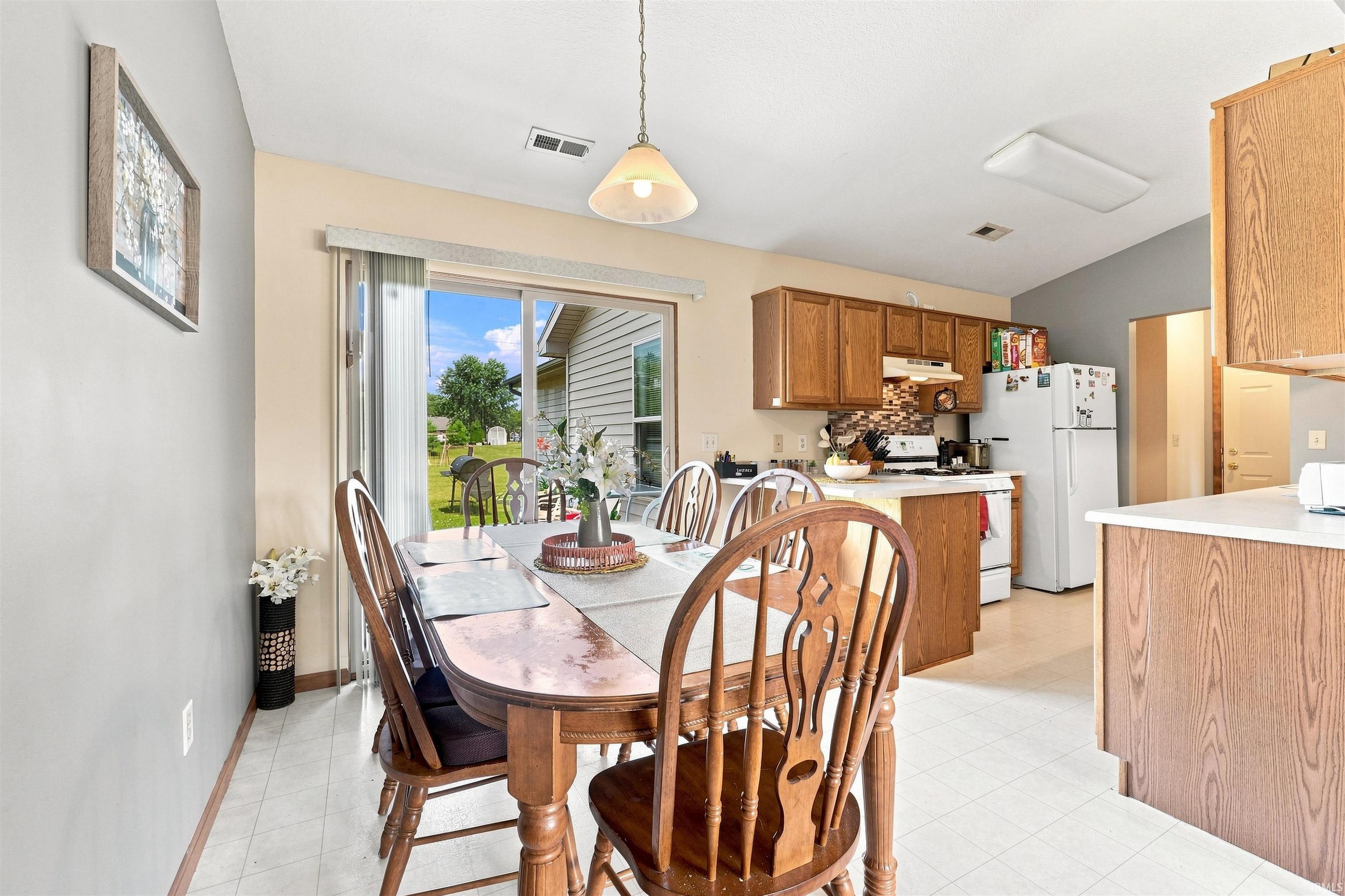 Bright and open dining and kitchen area featuring wood cabinetry, white appliances, and pendant lighting