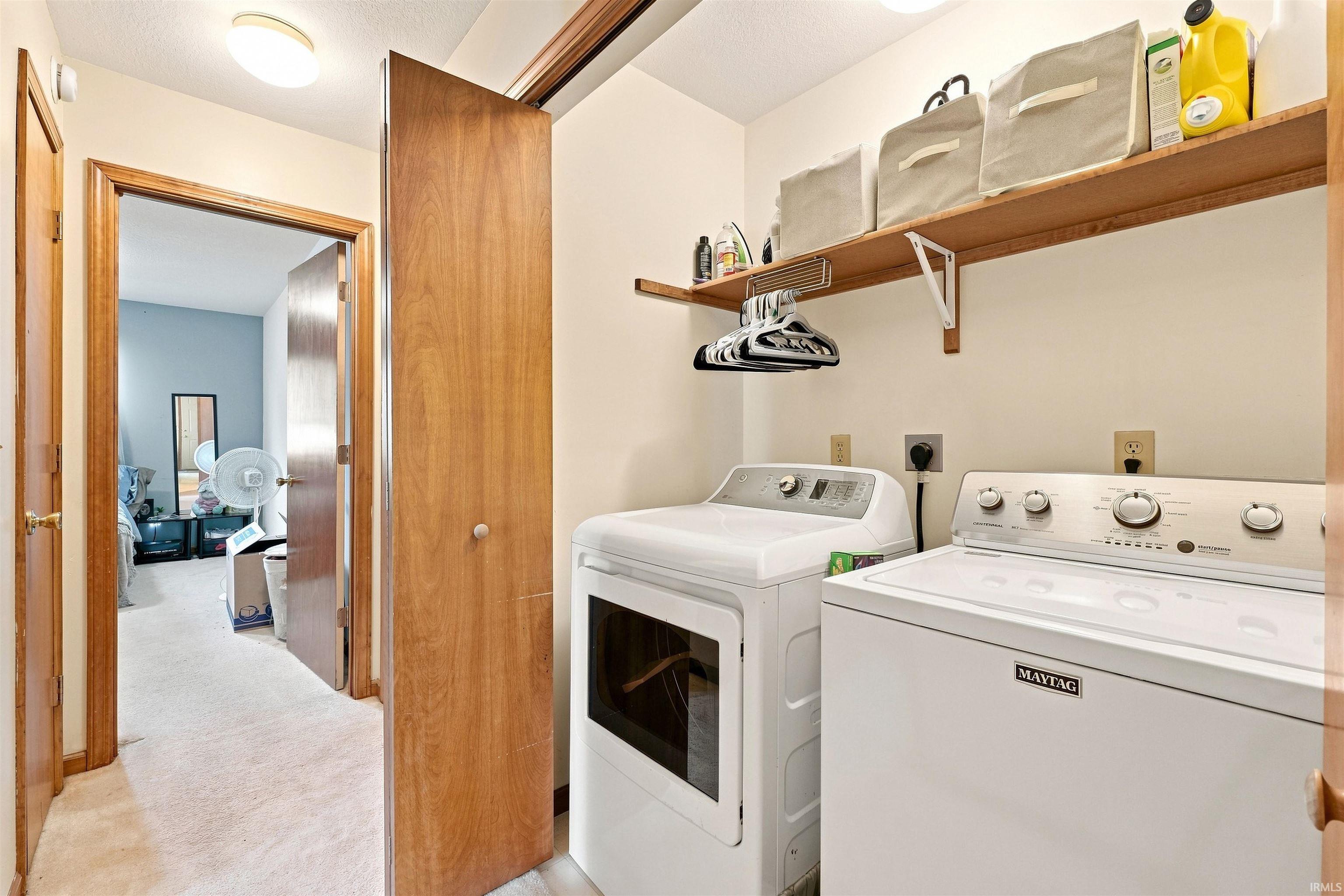 Dedicated laundry space featuring a white washer and dryer, integrated shelving, and a hanging rod