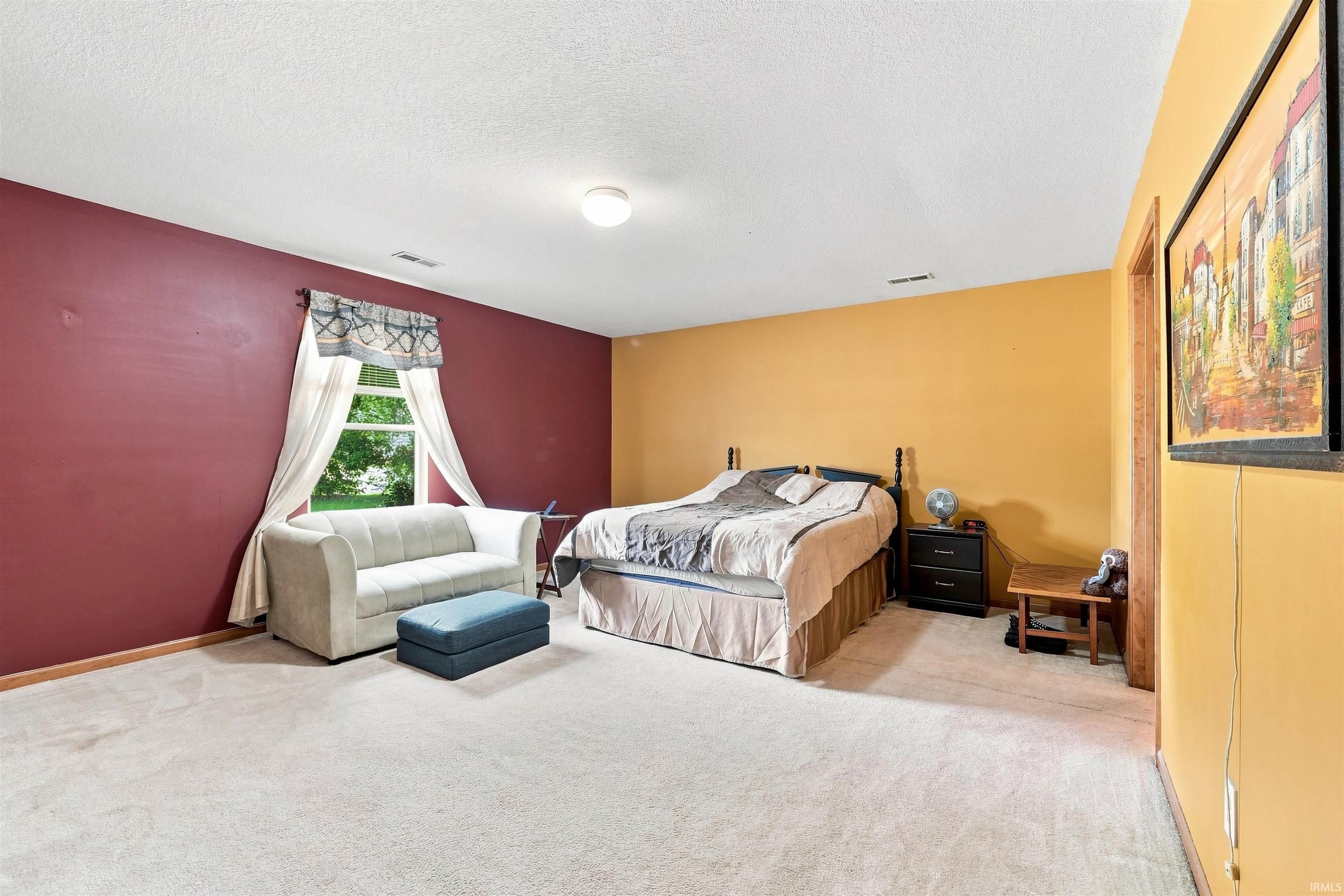 Spacious bedroom featuring neutral carpeting, a large window, and light-toned walls with a contrasting accent wall