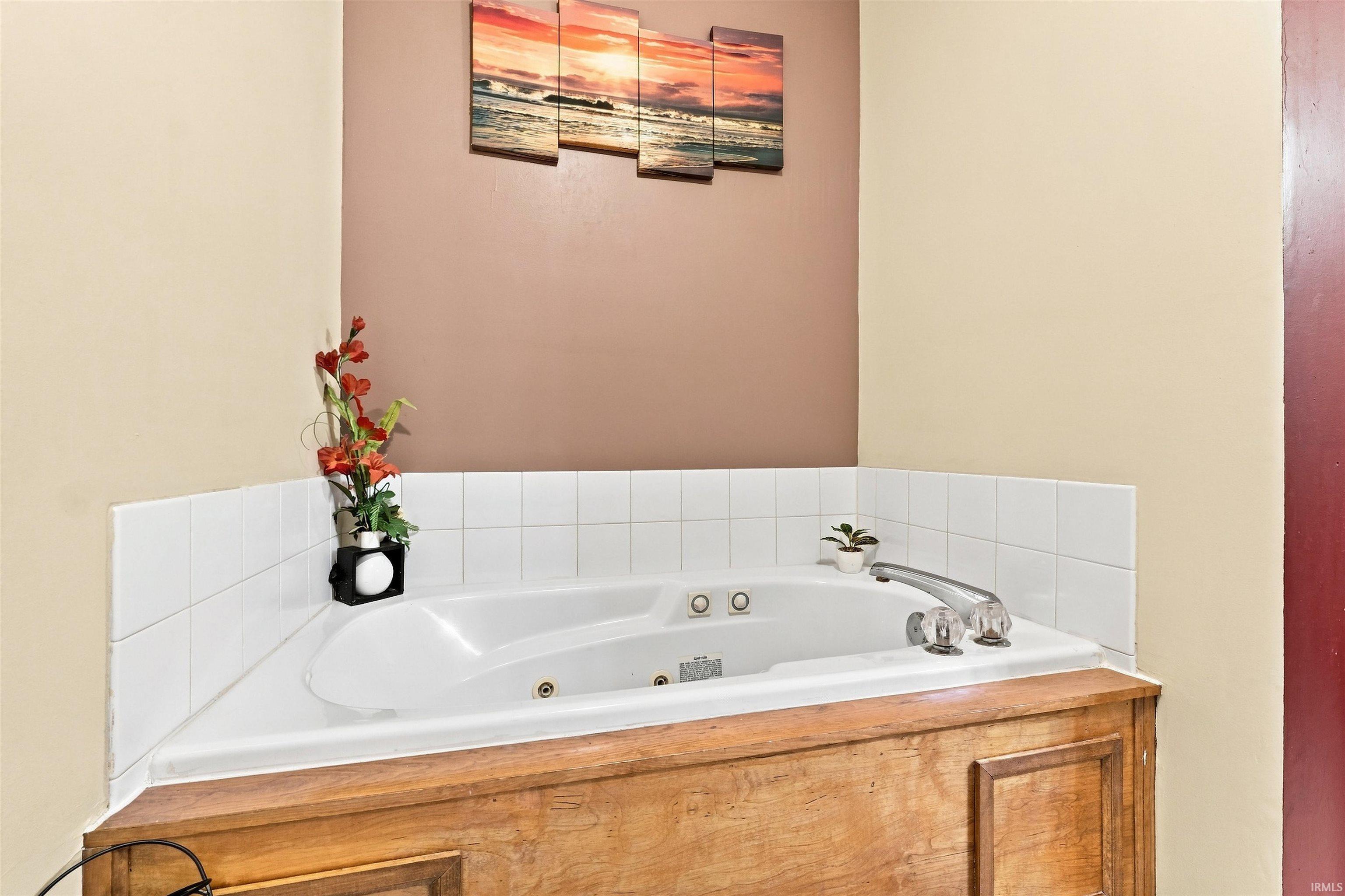 Corner jetted tub with white tile surround and a wood-finish base