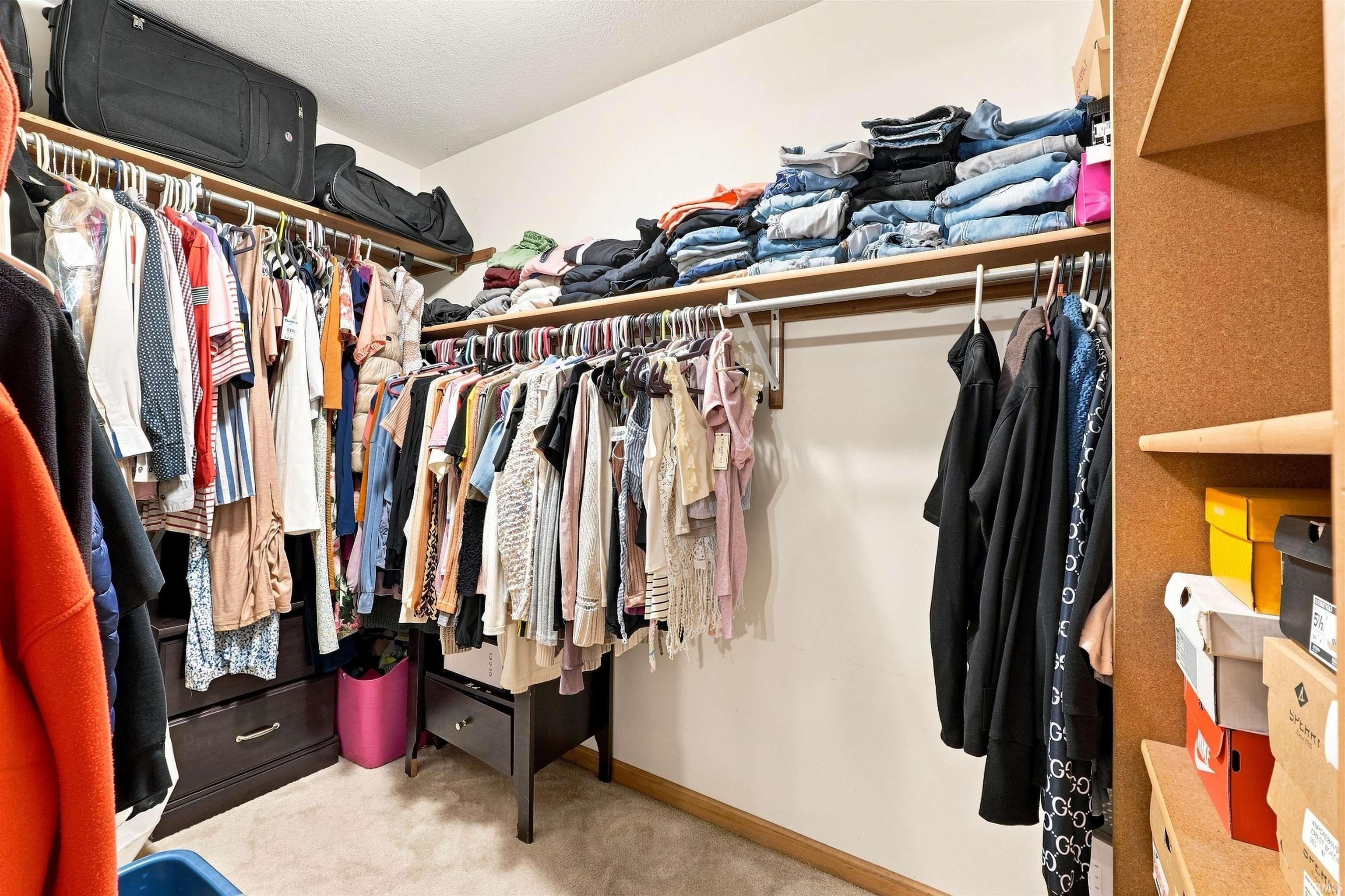 Walk-in closet featuring extensive built-in shelving, multiple hanging rods, corner drawer units, and carpet flooring