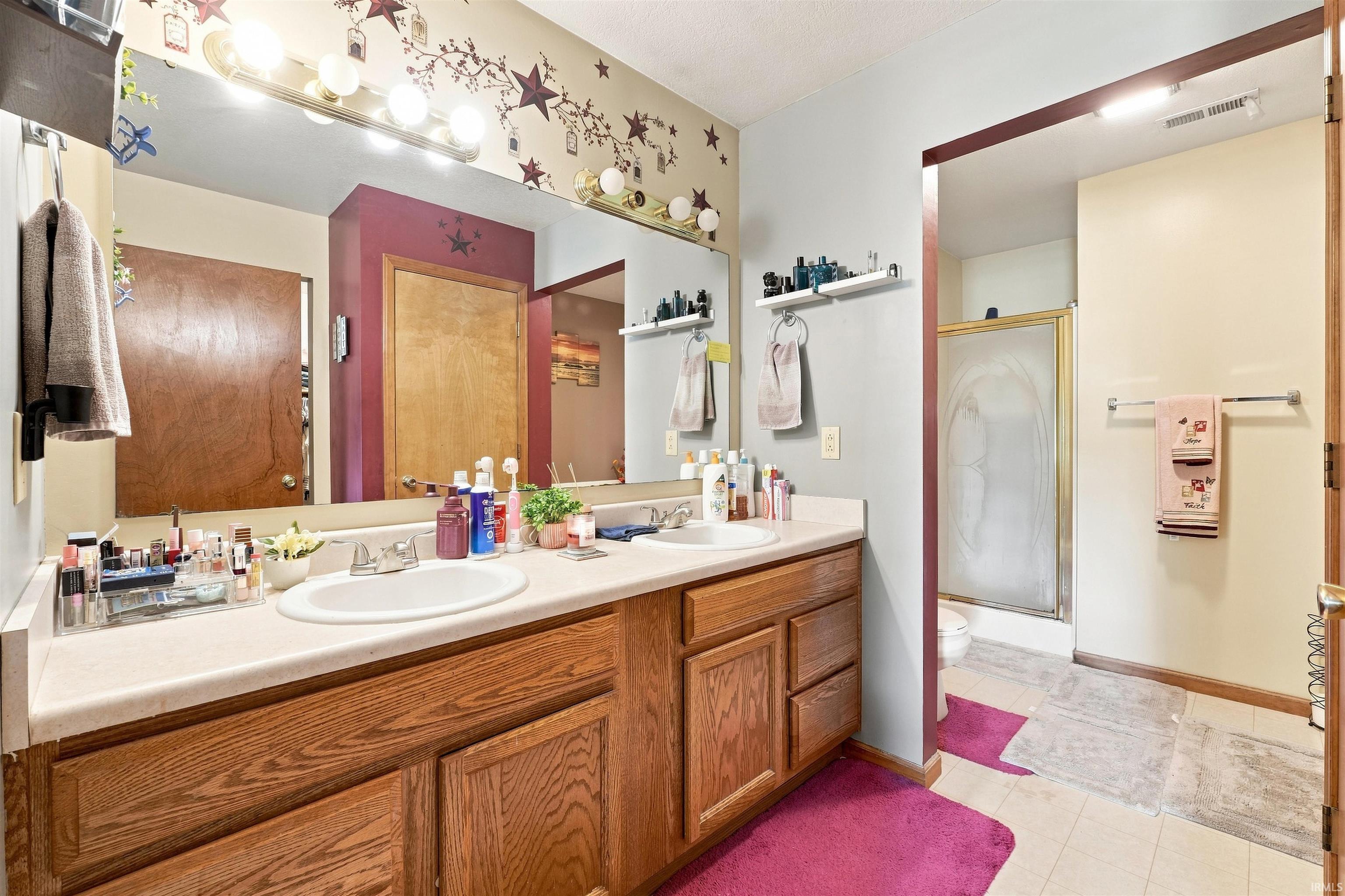 Bathroom featuring a dual-sink vanity with wood cabinetry, a large wall mirror, and overhead vanity lighting