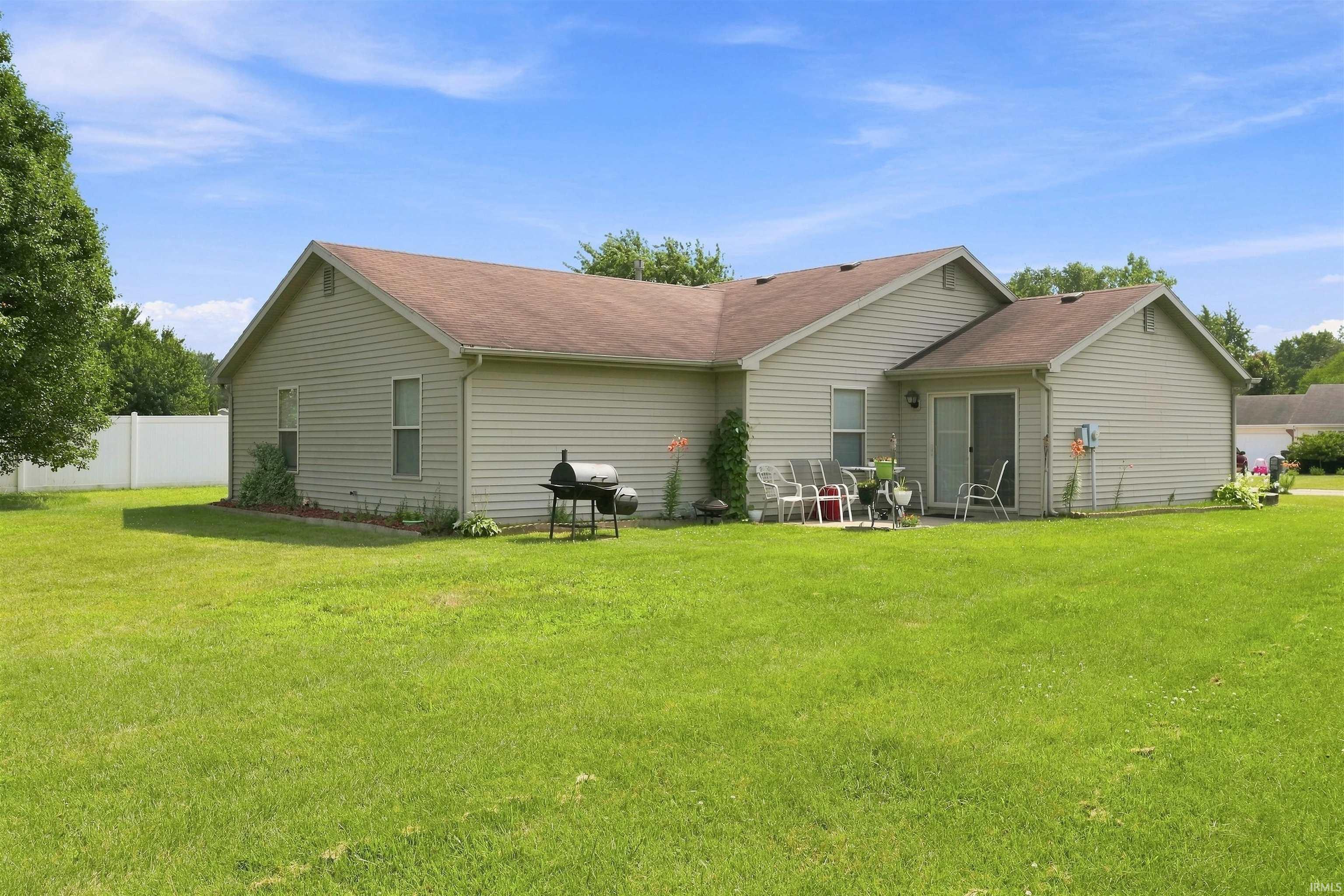 Expansive rear yard with a concrete patio, sliding glass door access, and vinyl siding exterior
