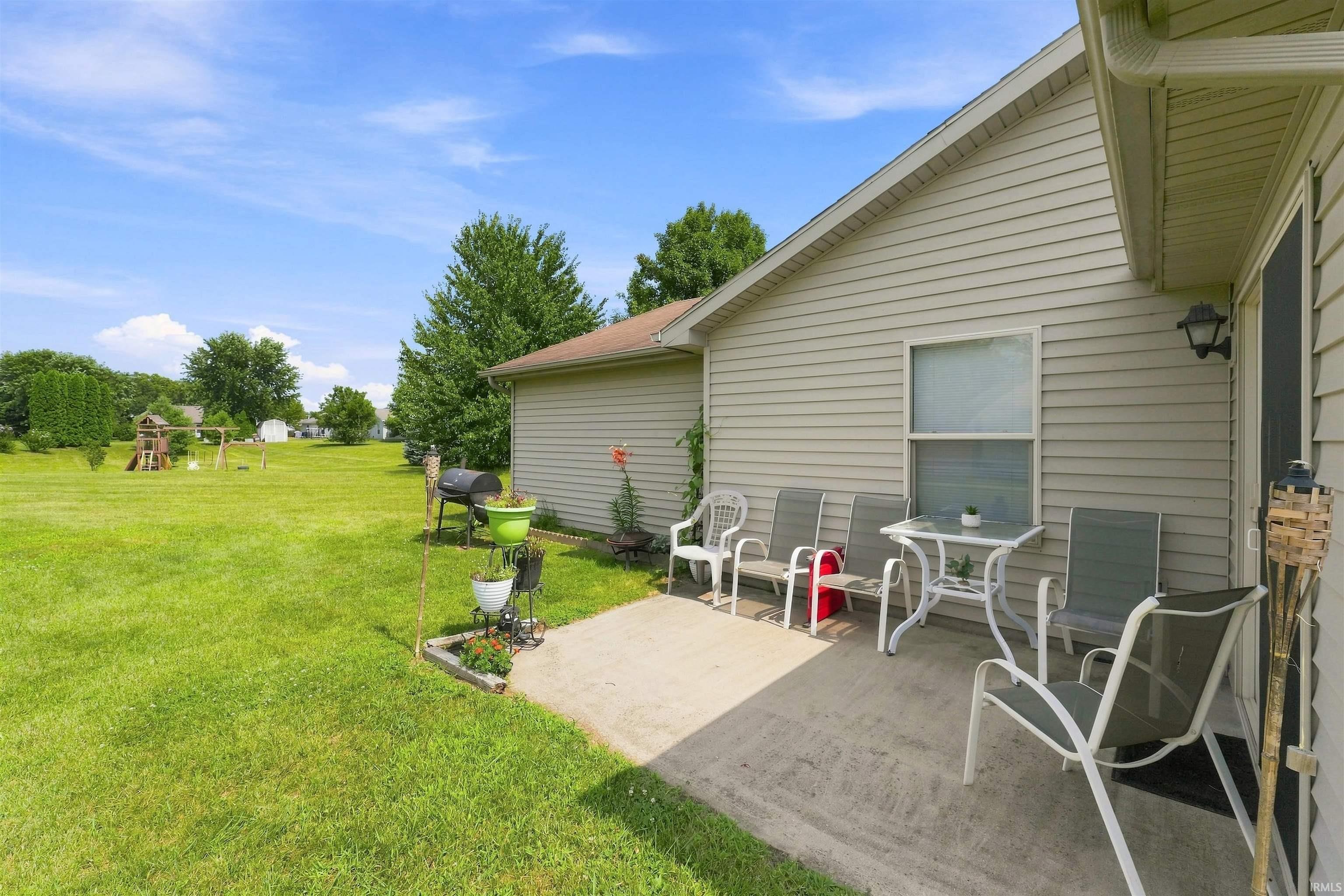 Expansive rear yard featuring a large concrete patio, light beige siding, and mature trees