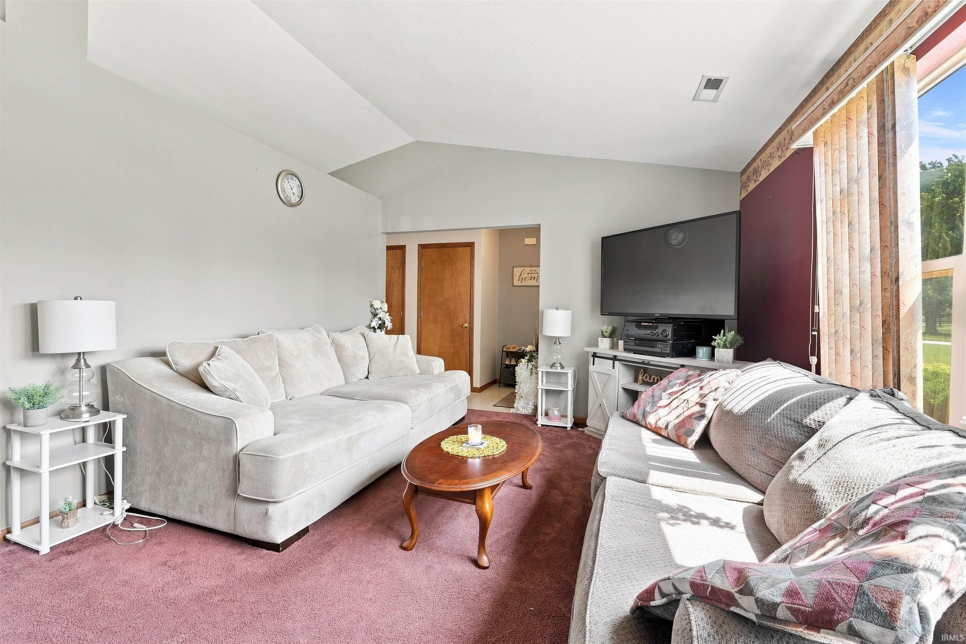 Spacious room featuring vaulted ceilings, a large picture window, and rich burgundy carpeting