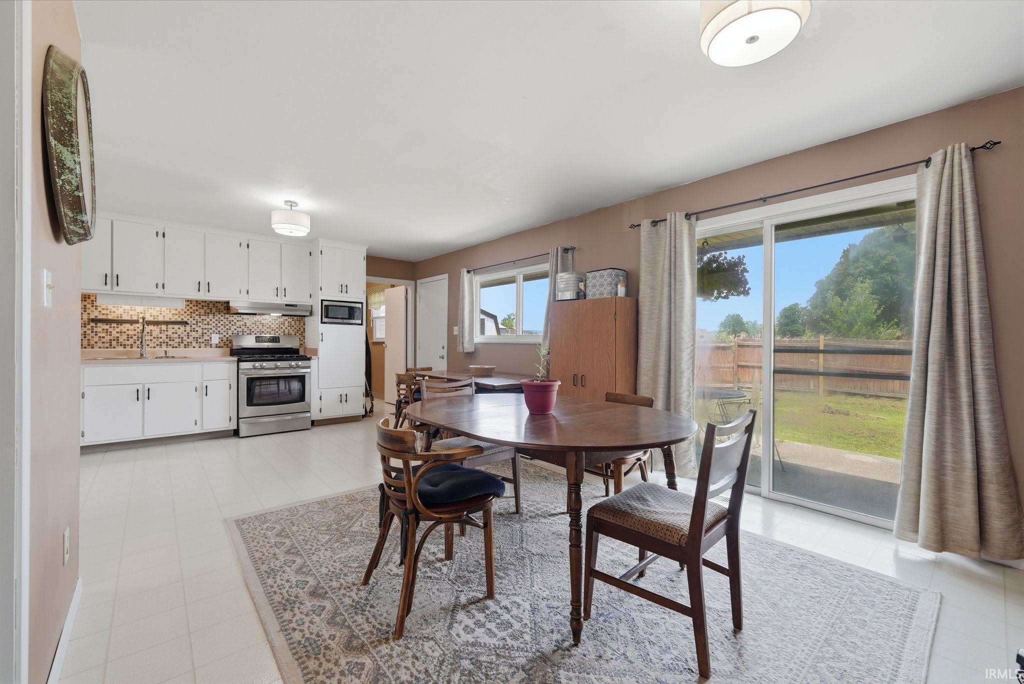 Open-concept kitchen and dining area featuring white cabinetry, mosaic tile backsplash, stainless steel range, and sliding glass doors to the backyard