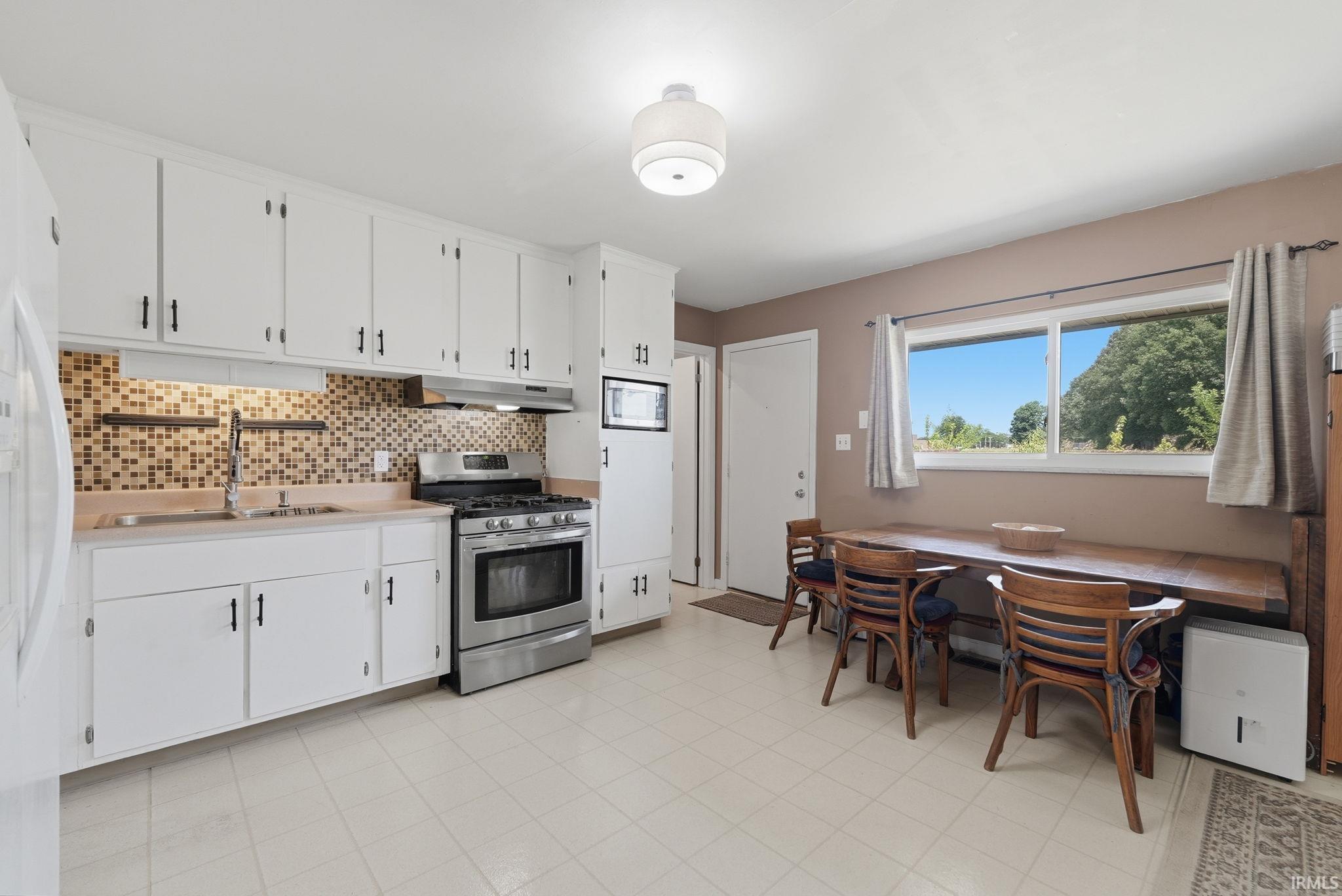 Kitchen featuring white cabinetry, a mosaic tile backsplash, stainless steel range, and a built-in microwave