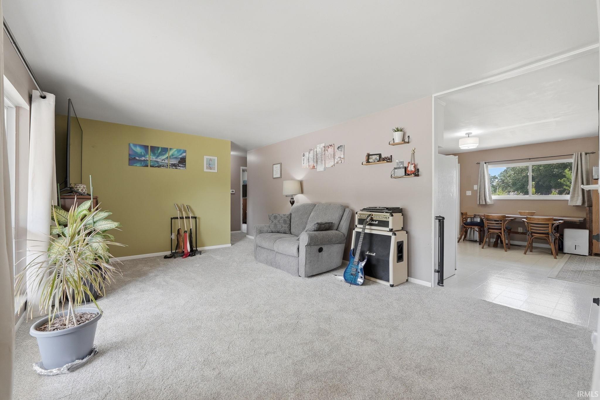 Expansive living area featuring light gray carpeting, a distinct accent wall, and an open entryway to an adjacent dining space