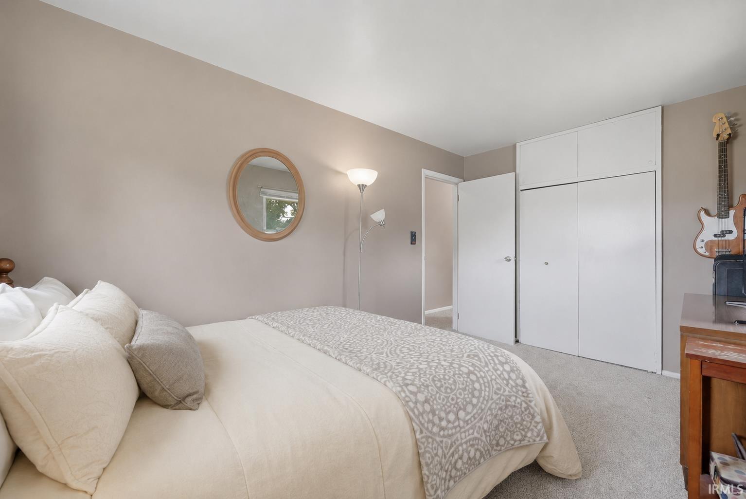 Neutral-toned bedroom featuring wall-to-wall carpeting and a mirrored closet with integrated overhead storage