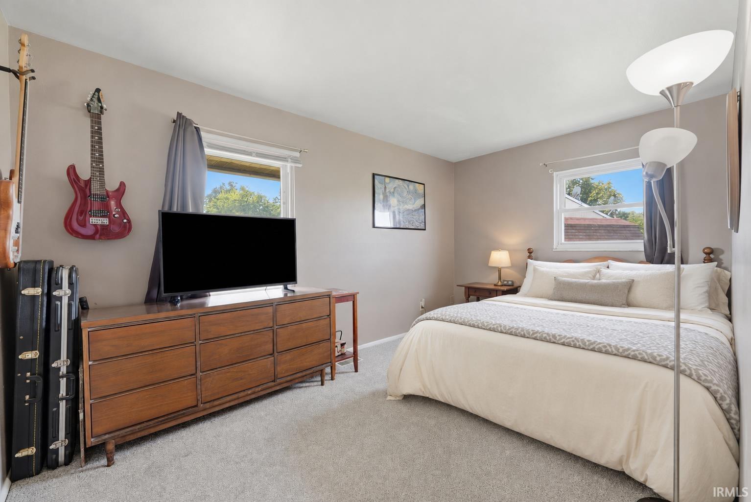 Bedroom featuring neutral wall paint, light gray carpeting, two large windows, and a wood-finish dresser