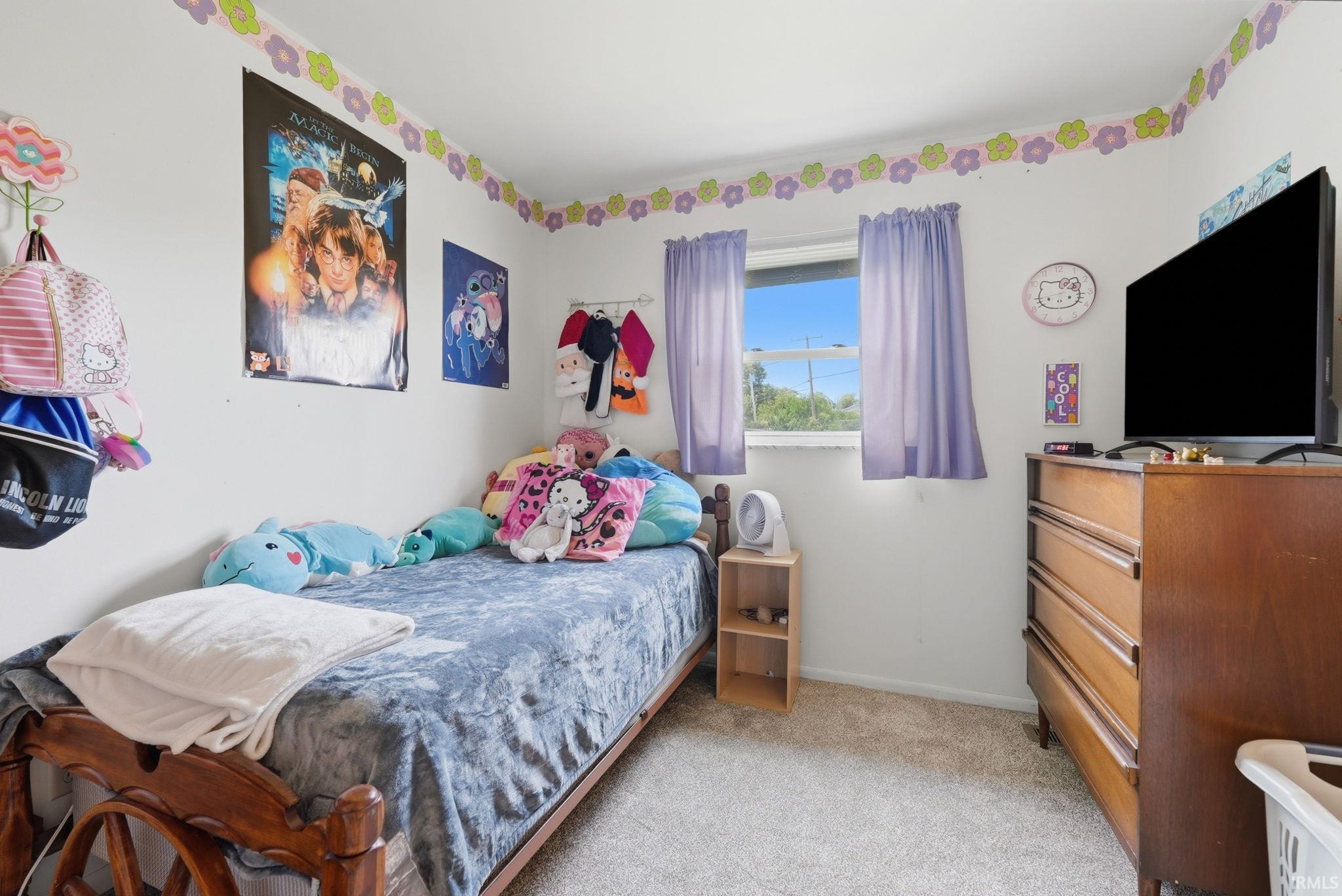 Bedroom featuring light-toned carpeting, white walls, and a window with purple drapes