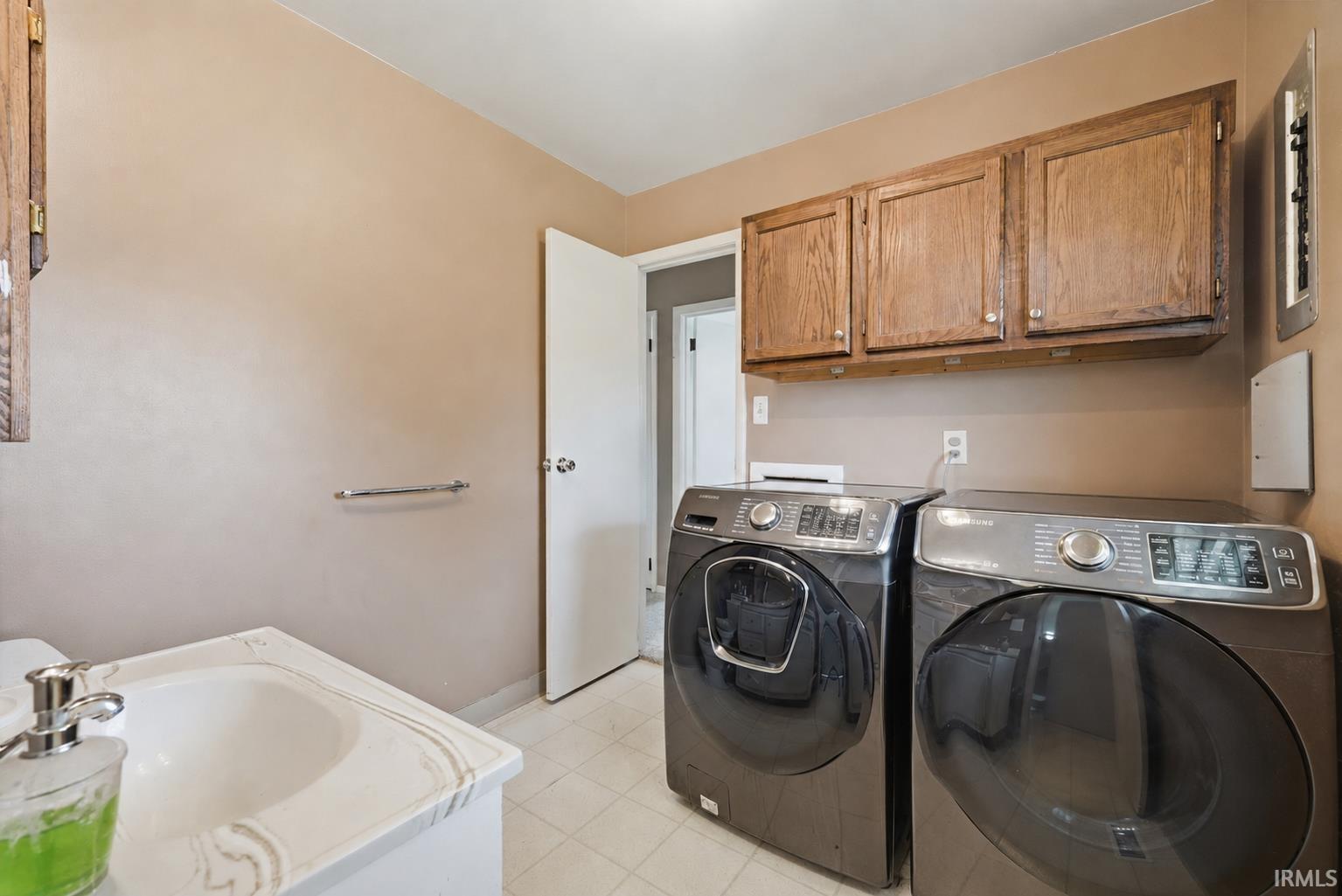 Dedicated laundry area featuring a built-in sink with a white countertop, overhead wood cabinetry, and tiled flooring