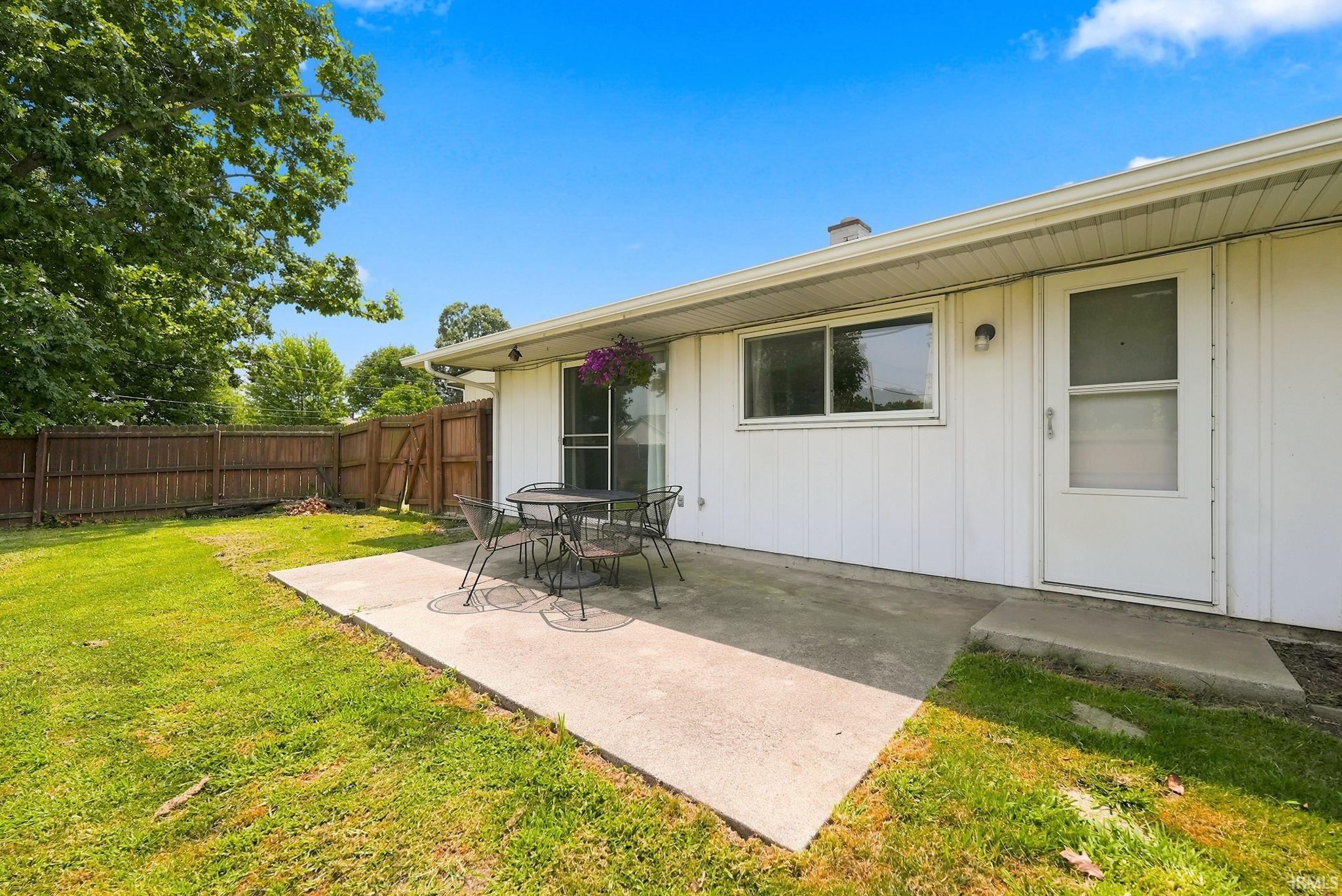 Rear concrete patio and lawn area featuring a tall privacy fence, white siding, and a screened door