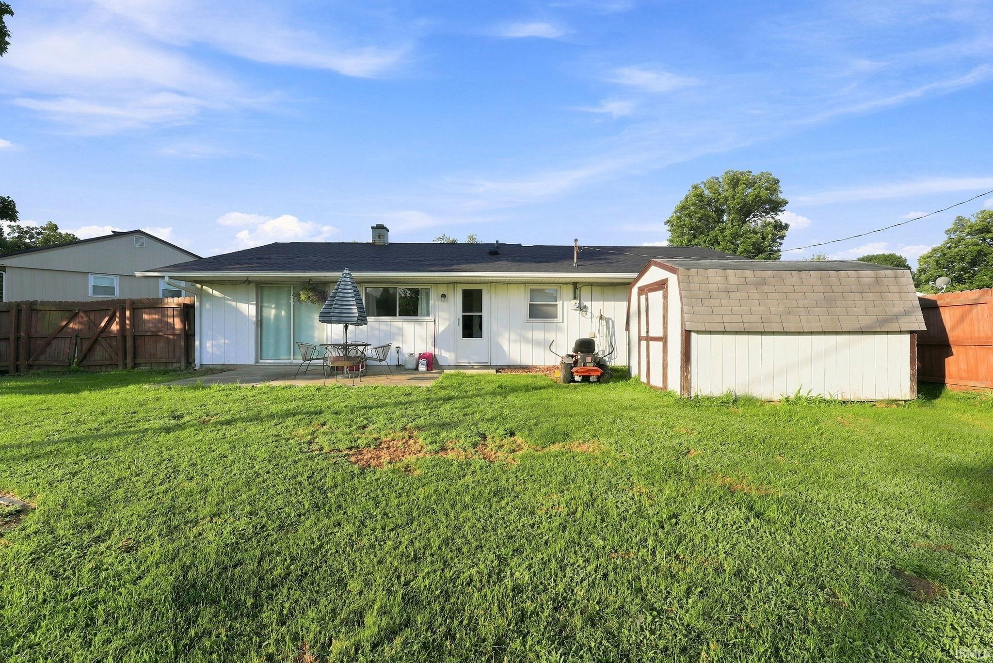 Expansive backyard featuring a large grass area, a patio space, and a storage shed with a shingled roof