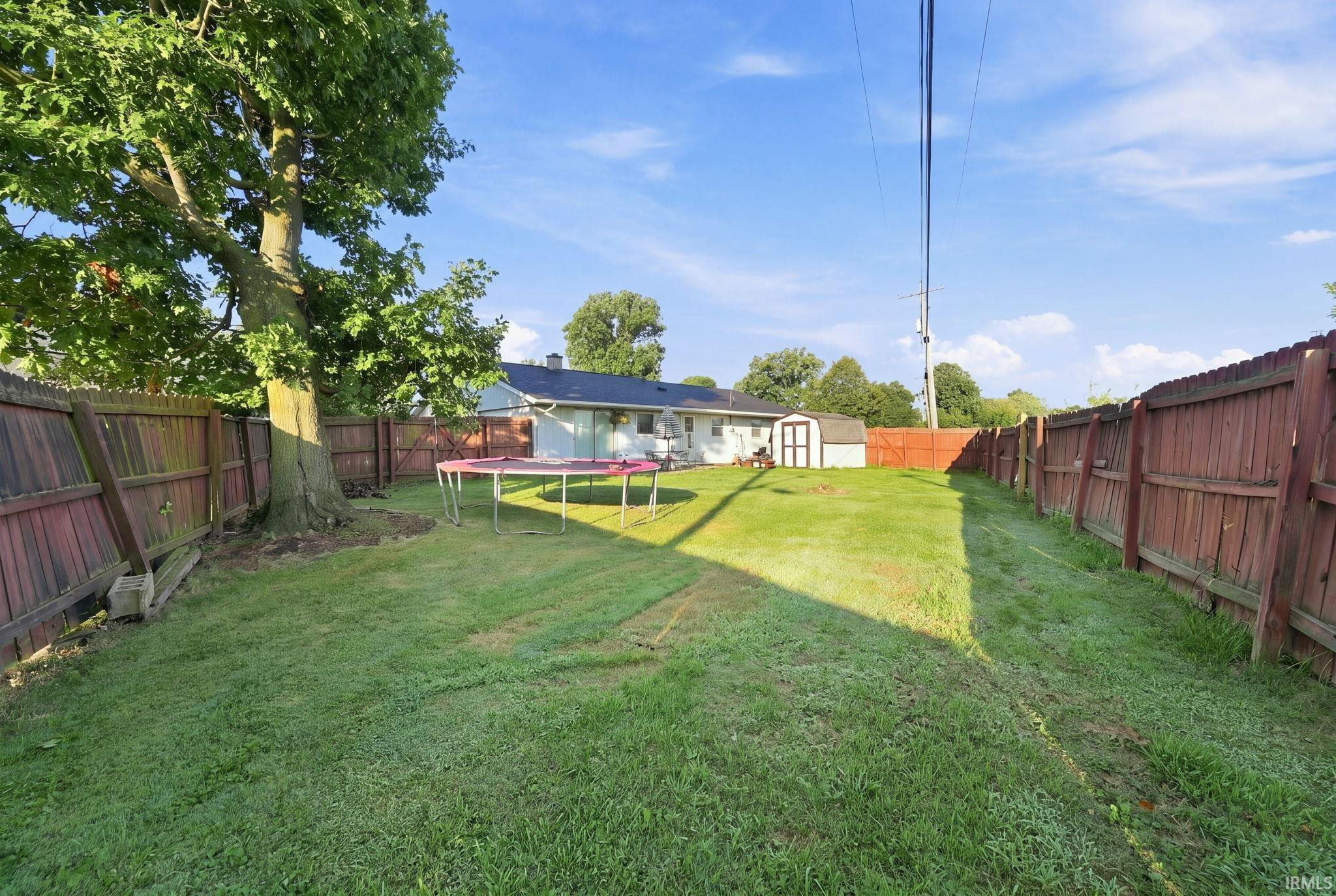 Spacious backyard featuring a substantial mature tree, a privacy fence, a detached storage shed, and a manicured lawn