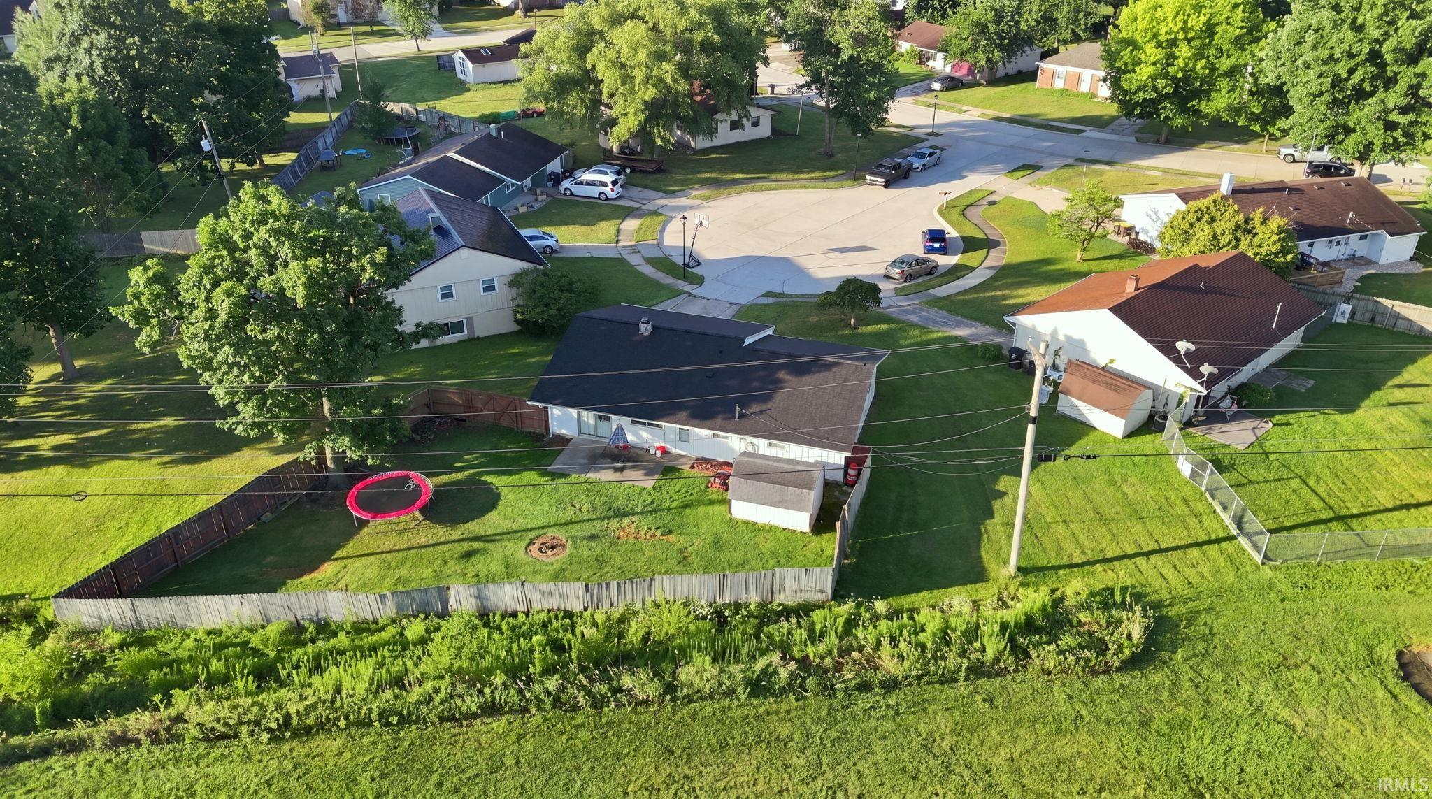 Expansive residential lot featuring a single-story home with dark roof, manicured lawn, mature landscaping, and established trees throughout the property