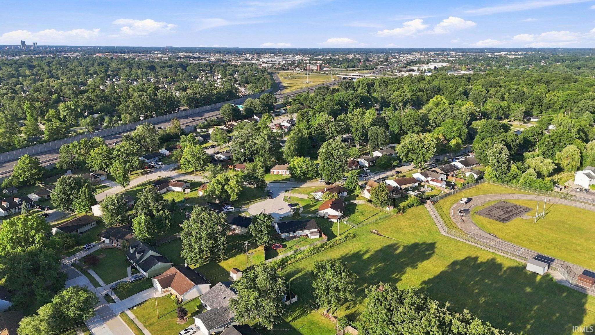 Aerial perspective showcasing a residential neighborhood with established trees, nearby highway access, and a recreation field