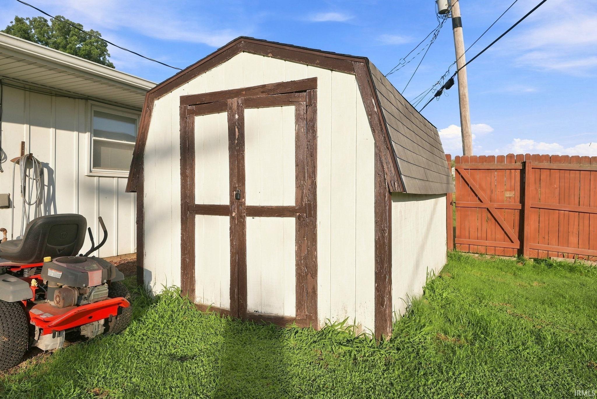 Gambrel-style storage shed with double doors and a shingled roof, featuring a painted wood exterior