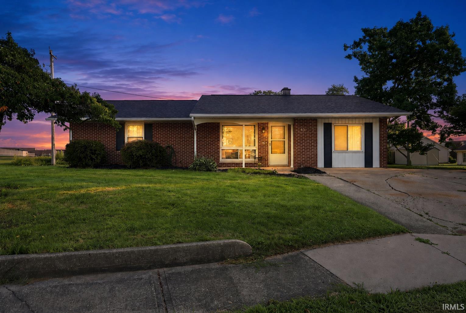 Brick ranch-style residence featuring a dark shingle roof, well-maintained front lawn, and mature landscaping