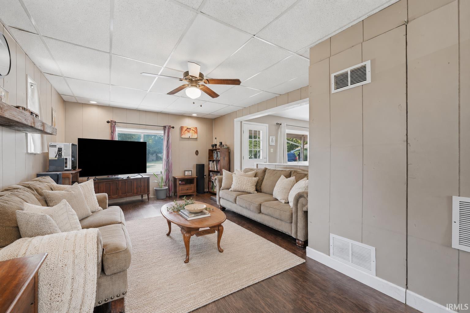 Spacious living area featuring wood-finish flooring, a ceiling fan, and paneled walls