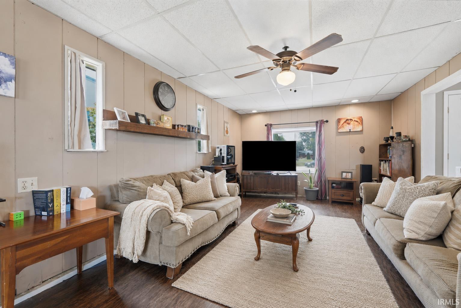 Spacious living area featuring wood-finish flooring, a ceiling fan with integrated lighting, and multiple windows