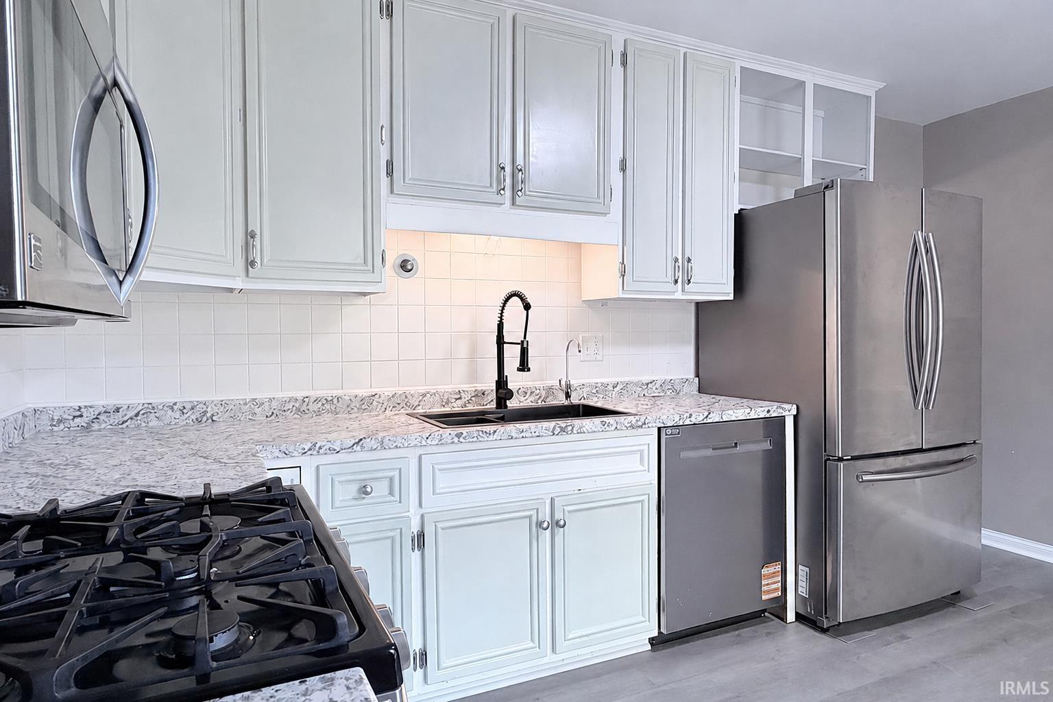Kitchen featuring white cabinetry, granite-patterned countertops, a stainless steel refrigerator, a black gas range, and wood-finish flooring