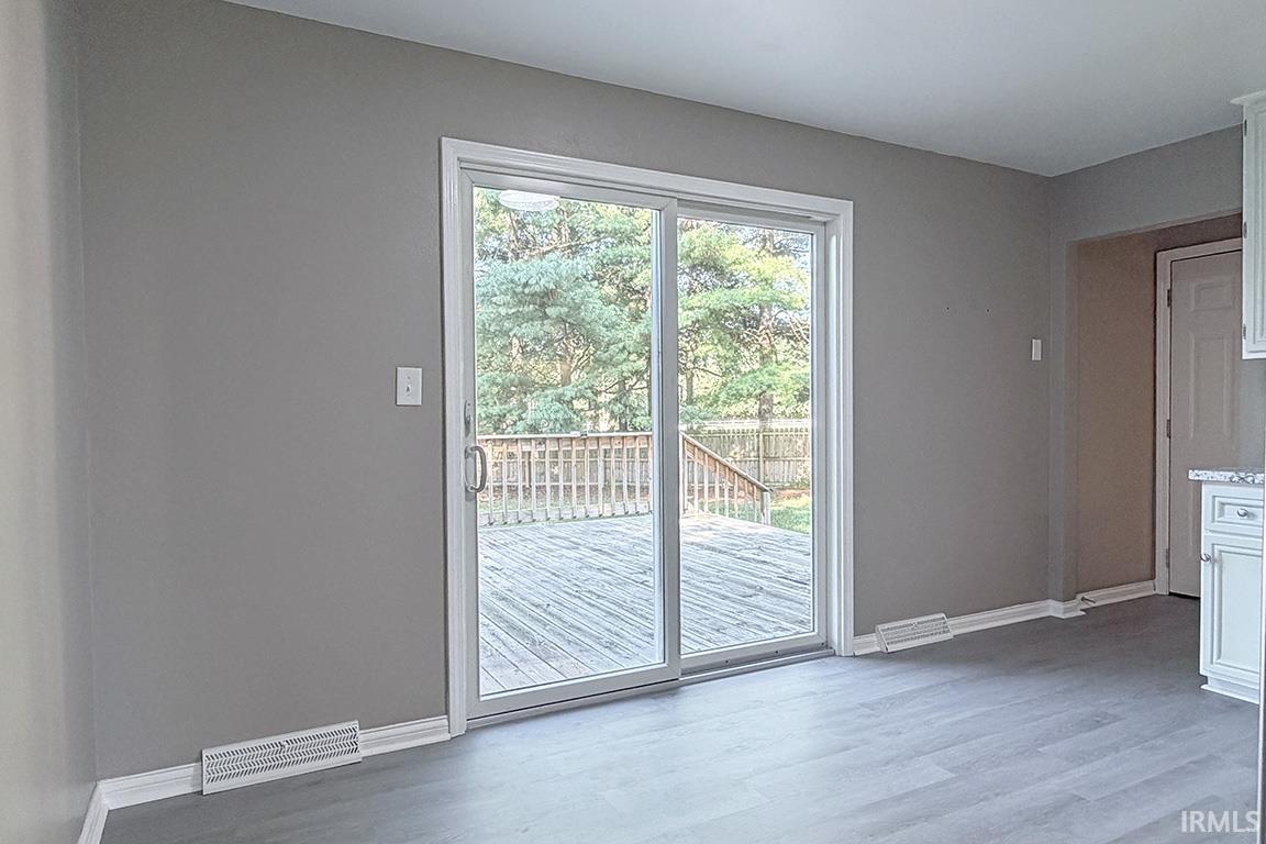 Sliding glass doors opening to a wood deck, featuring wood-finish flooring, neutral wall paint, and white baseboards
